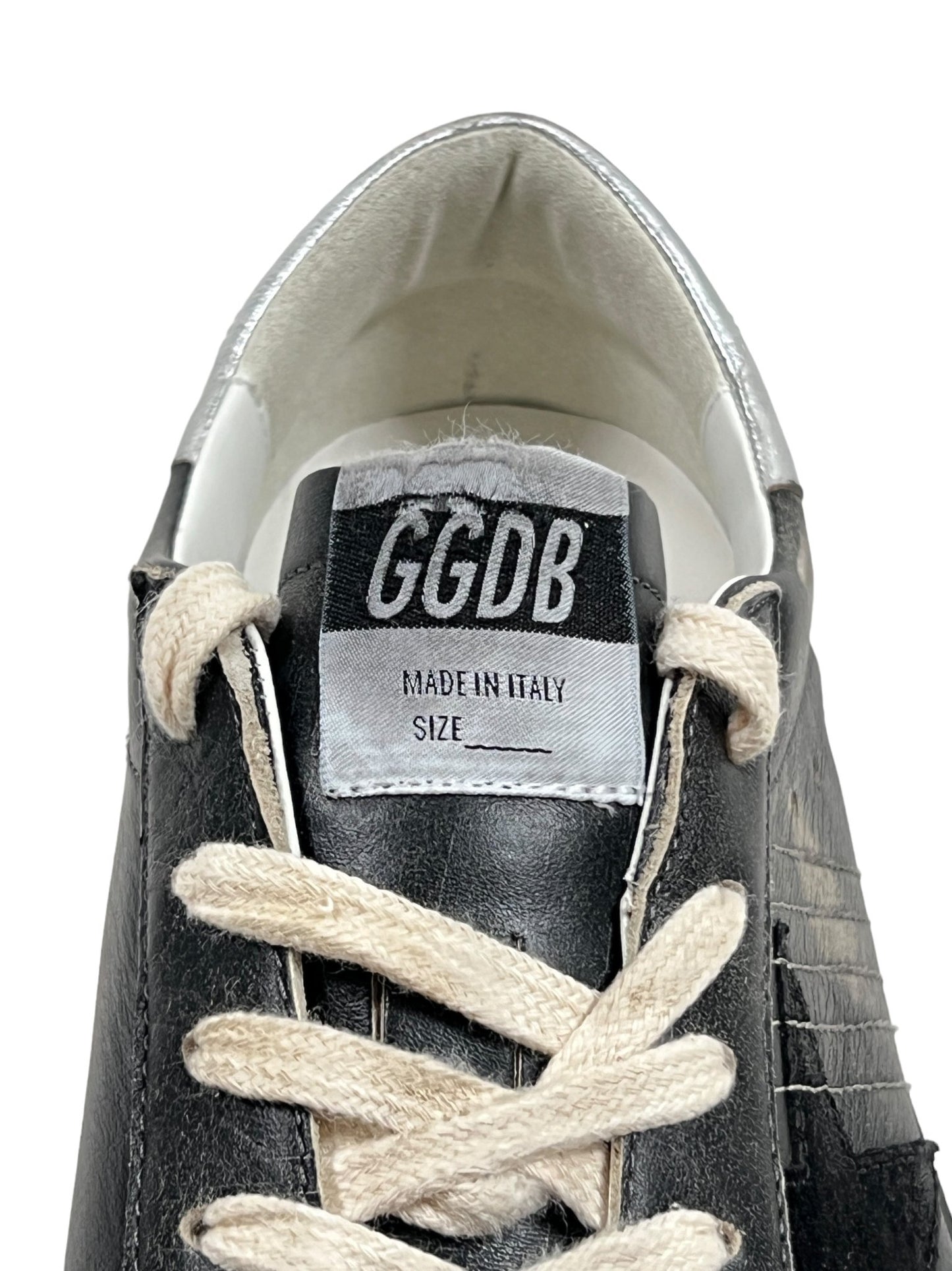 Close-up of the GOLDEN GOOSE GMF00290 SUPER STAR LEATHER BLACK SILVER sneaker, showcasing its black silver leather design with white laces, a label reading "GGDB MADE IN ITALY," and a blank space for the size information.