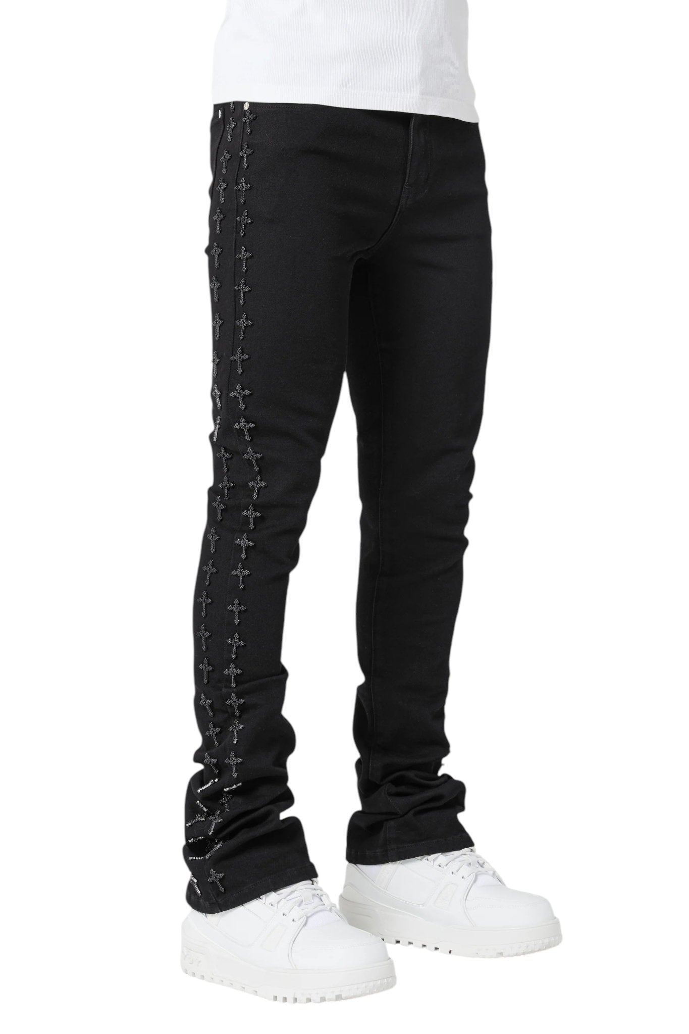 Front view of a person donning GUAPI's Guapi All Black Crosses Embellished Denim, featuring a slim tapered fit, paired with white sneakers for a streetwear look.