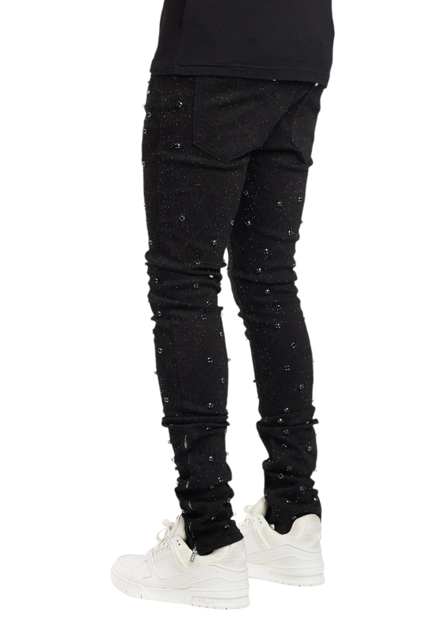 A person wearing GUAPI ALL BLACK EMBELLISHED DENIM and white sneakers stands with their back to the viewer.