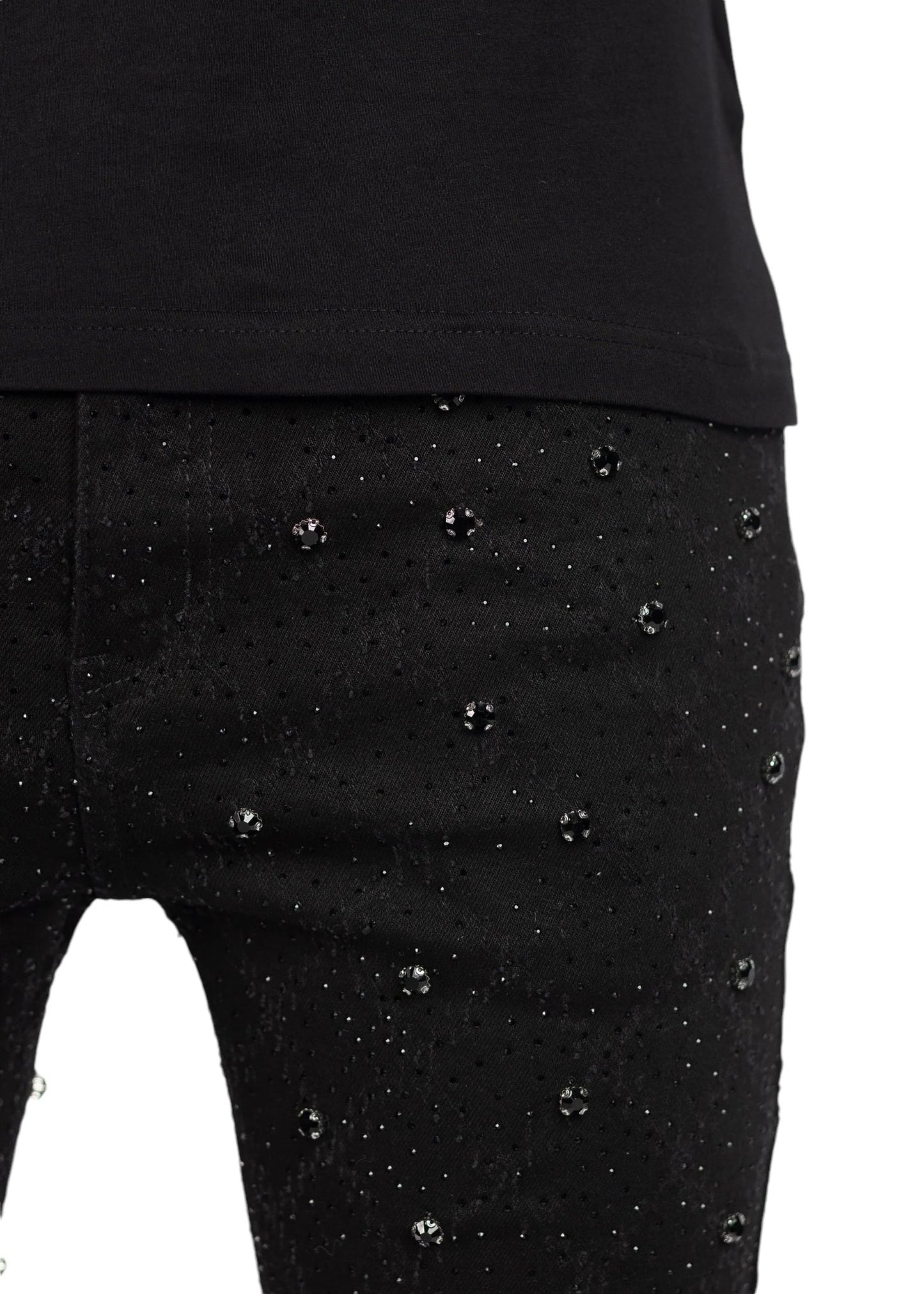 Close-up of a person wearing GUAPI ALL BLACK EMBELLISHED DENIM by GUAPI, featuring perfectly fitted black pants adorned with small shiny studs.