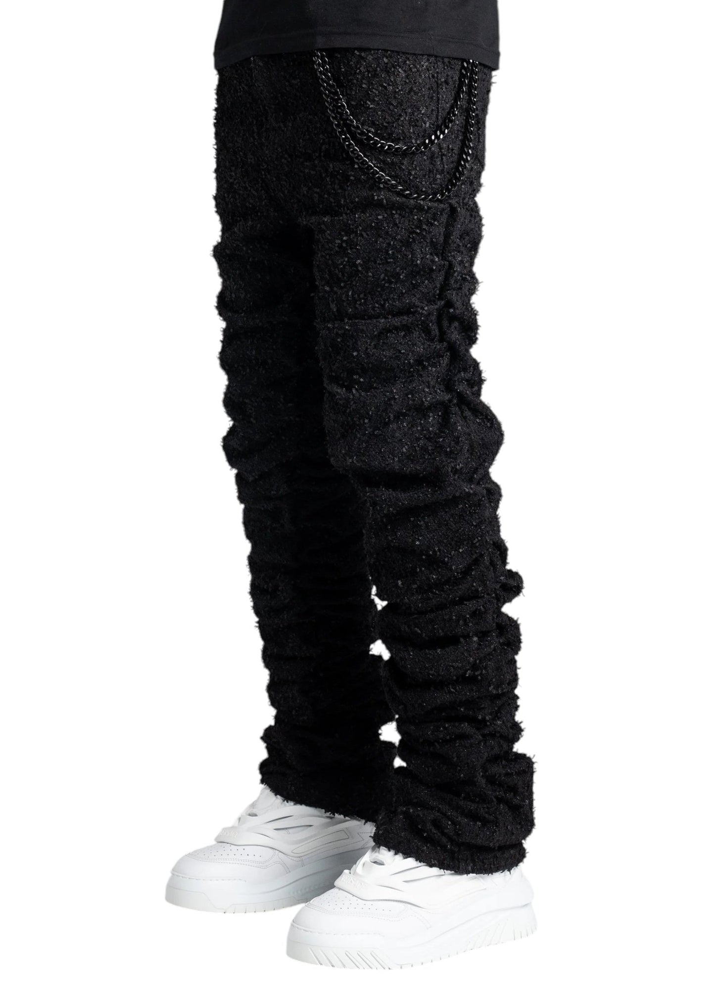 A person wearing the Guapi All Black Super Stacked Denim with a tapered fit and white shoes, elegantly adorned with chains hanging from the waist.