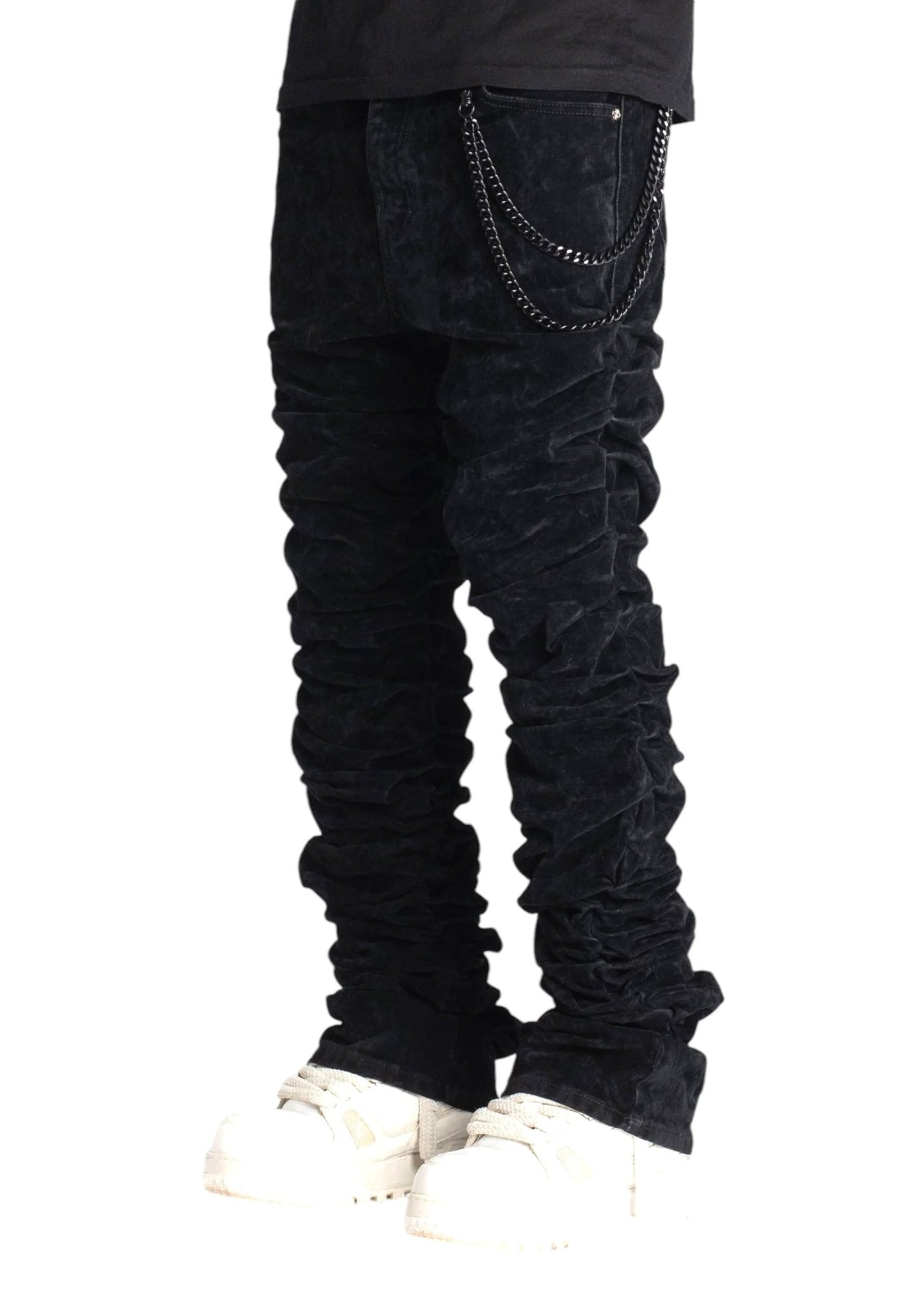 A person wearing the Guapi All Black Super Stacked Denim V2 from GUAPI, featuring chain details and white shoes, highlights a tapered fit that accentuates the luxury fabrics.