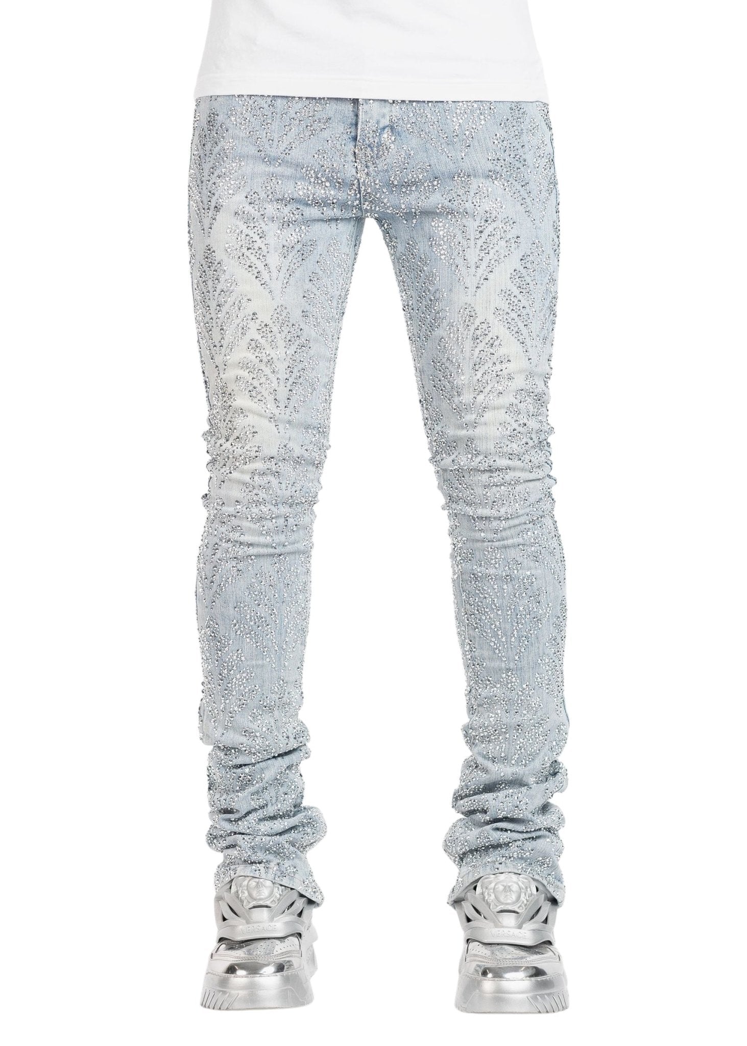 Dressed in the GUAPI Aqua Blue Embellished Denim V2 and silver metallic sneakers, a person stands elegantly against a white background, capturing the essence of luxury fashion.