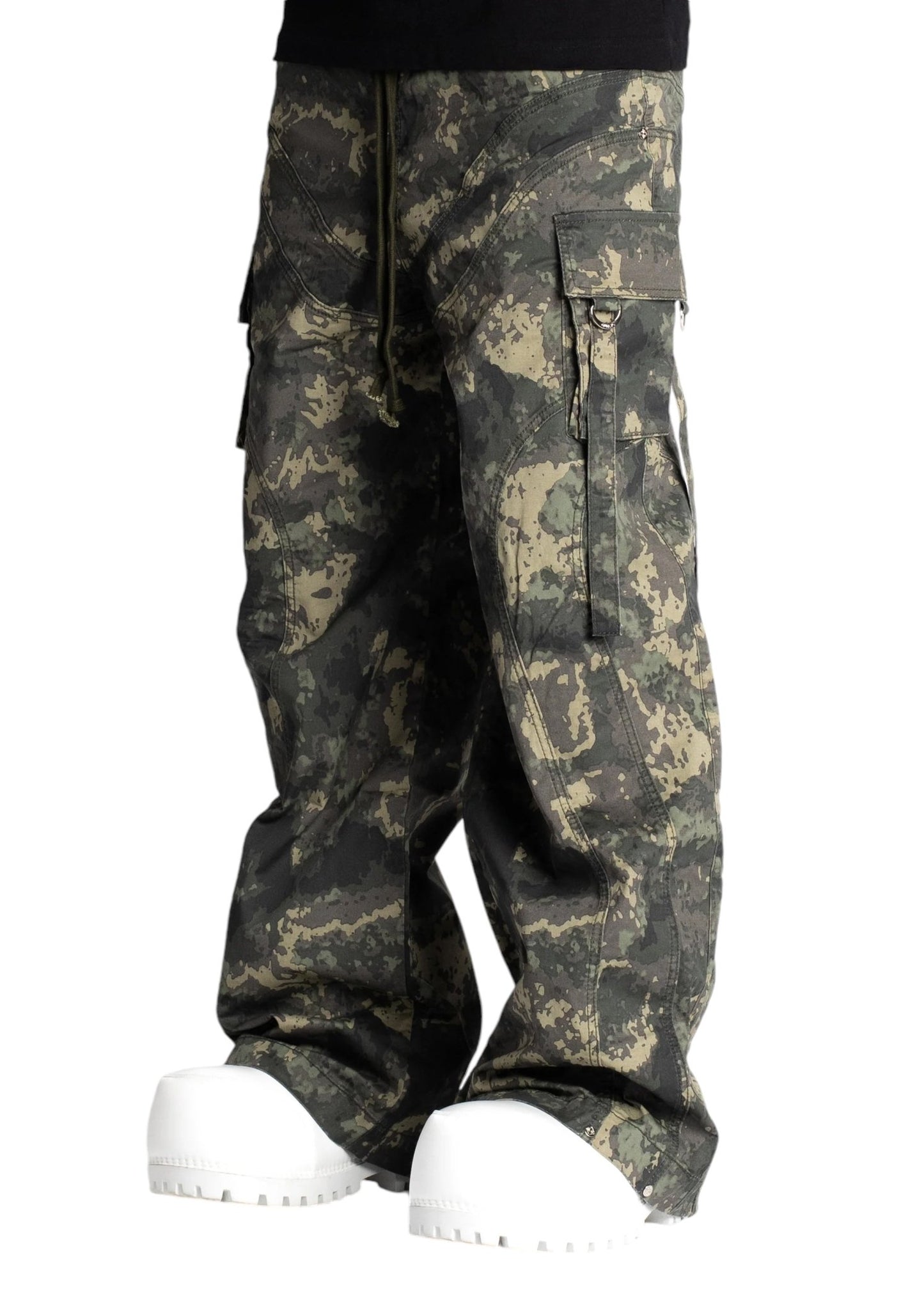 A person sporting a streetwear look with the Guapi Camo Extra Baggy Cargos V3 from GUAPI and a pair of white boots.