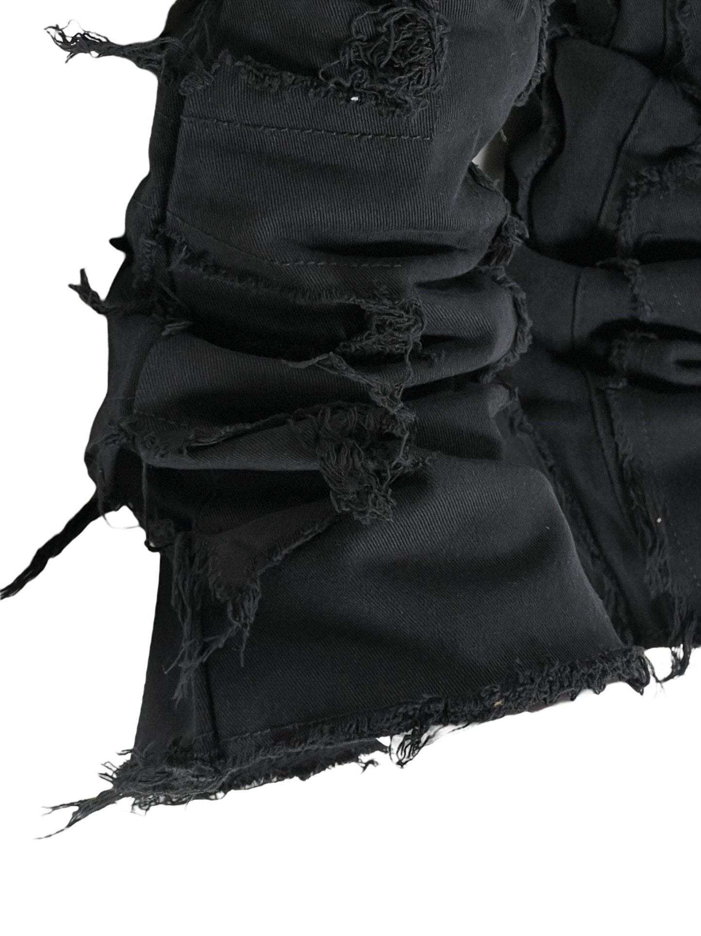 Close-up of a GUAPI OBSIDIAN BLACK BLOOD DIAMOND STACKED DENIM garment with distressed and frayed fabric textures.
