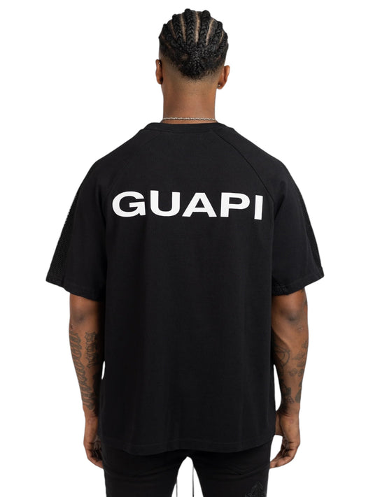 Back view of a person wearing the Guapi Obsidian Black Half Moon Tee by GUAPI, made from 100% cotton, featuring "GUAPI" printed in white on the back with subtle applique detailing.