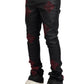 The person is wearing GUAPI's limited edition Obsidian Black Icon Embellished Denim V2 with red diamond accents, paired with white sneakers, against a plain background.