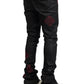 A person wears GUAPI's Obsidian Black Icon Embellished Denim V2 featuring red diamond patterns, paired with white sneakers, standing against a plain backdrop.