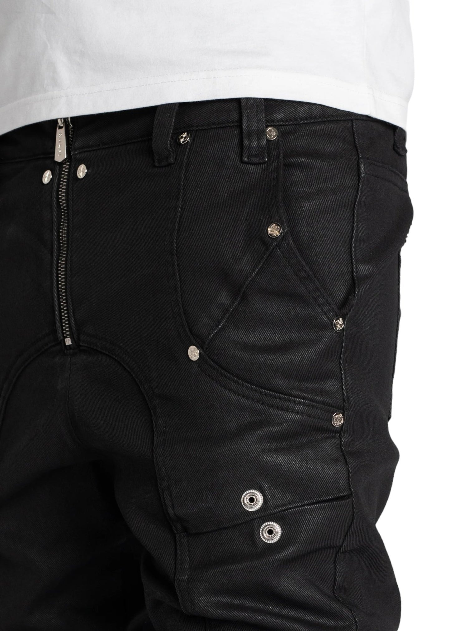 Close-up of a person's midsection wearing GUAPI OBSIDIAN BLACK WAXED PREMIUM DENIM V2 jeans with multiple silver buttons and zippers, paired with a white shirt.