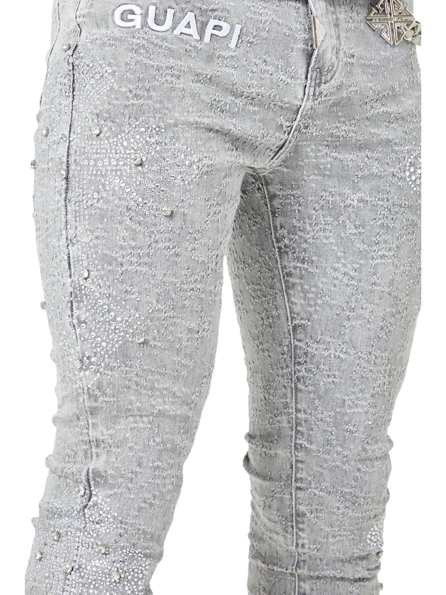 Close-up of a person in GUAPI’s Smoke Grey Distressed Cross Denim, featuring rhinestone cross details and "GUAPI" branding near the waistband.
