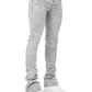 Model wearing GUAPI Smoke Grey Distressed Cross Denim stacked jeans with rhinestone cross details and chunky white sneakers, set against a plain background.
