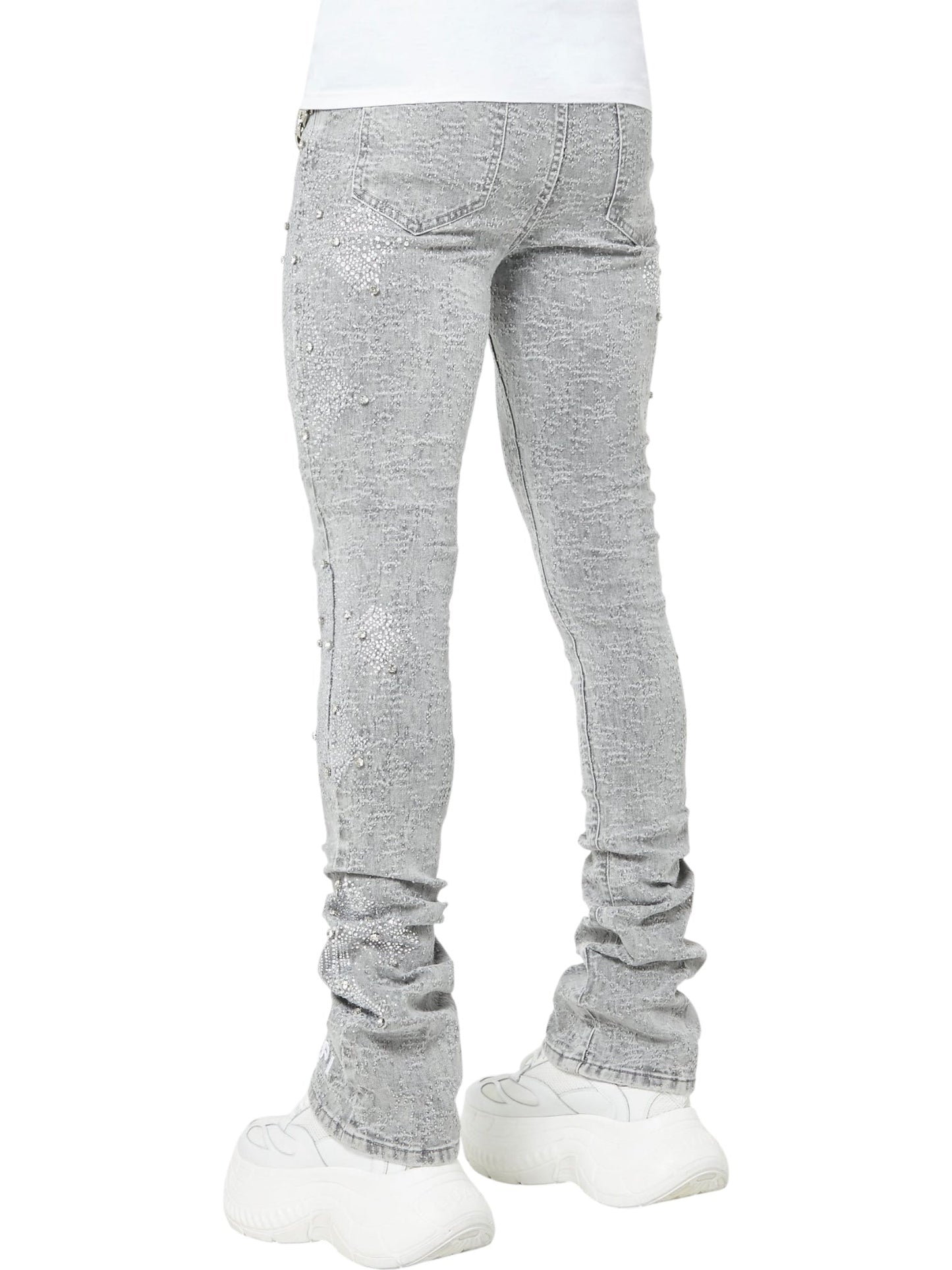 Person wearing GUAPI’s Guapi Smoke Grey Distressed Cross Denim skinny jeans with subtle embellishments, styled with chunky white sneakers, seen from the back against a plain white background.