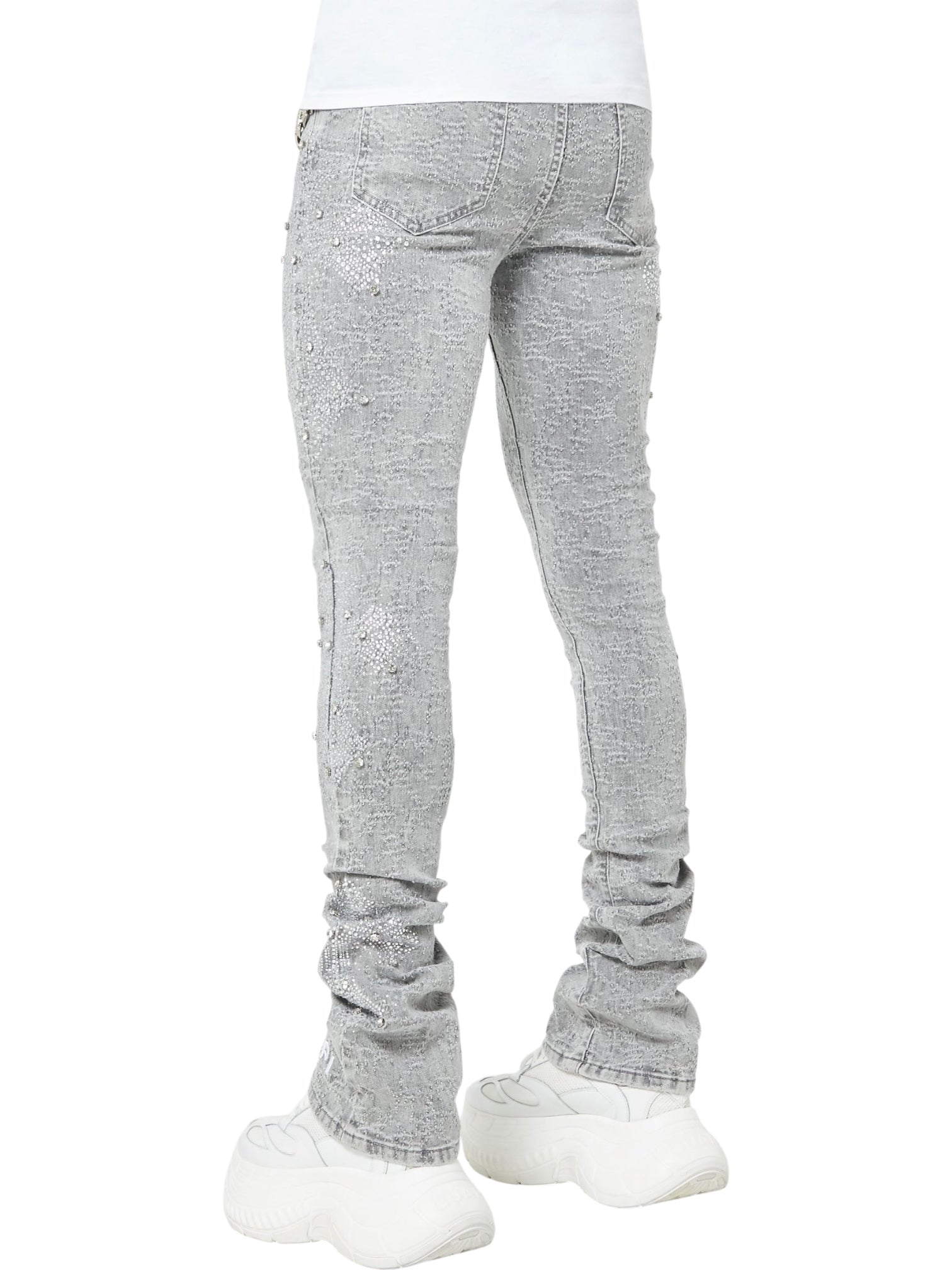 Person wearing GUAPI’s Guapi Smoke Grey Distressed Cross Denim skinny jeans with subtle embellishments, styled with chunky white sneakers, seen from the back against a plain white background.