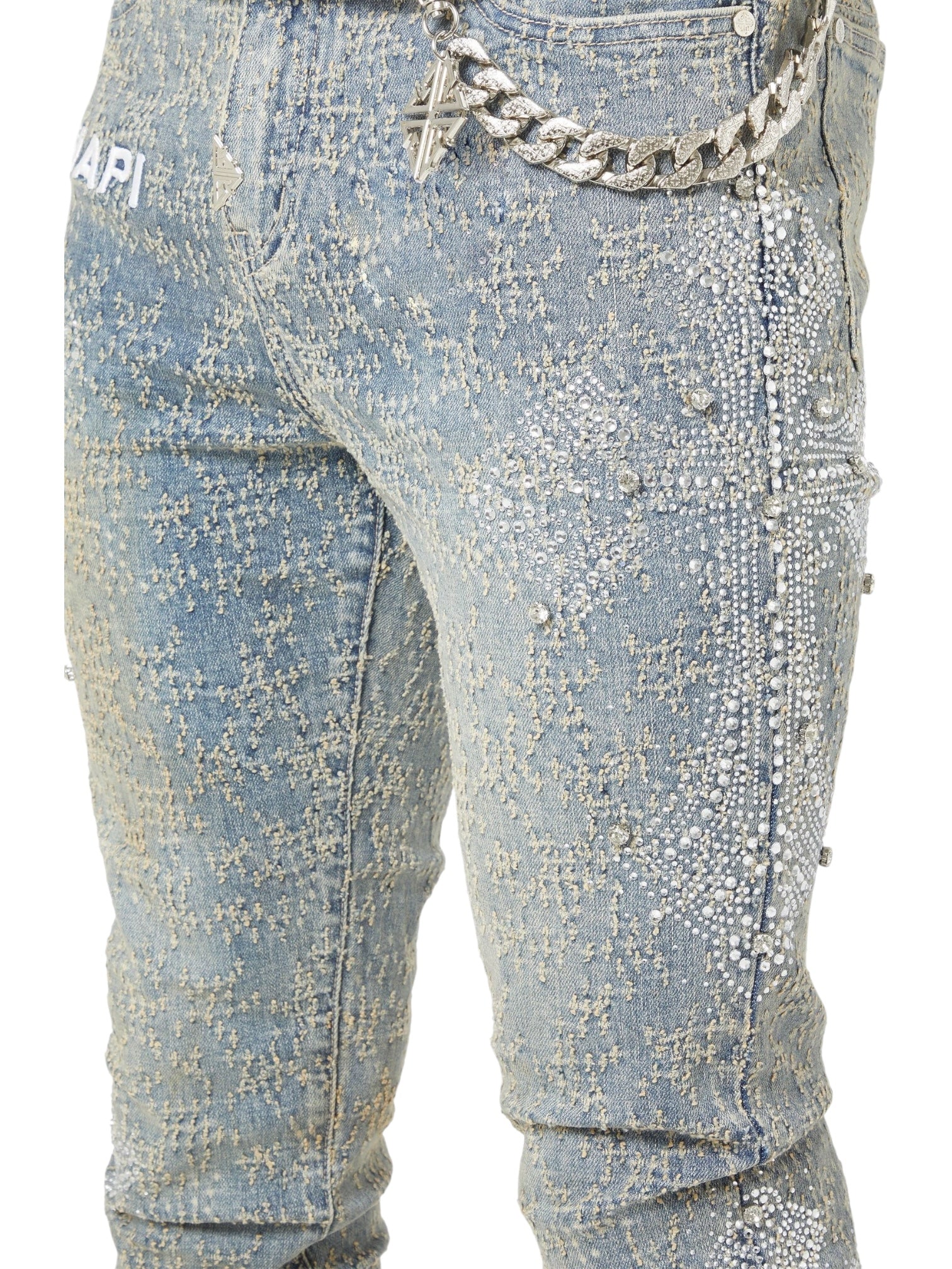 Close-up of GUAPI’s Vintage Blue Distressed Cross Denim featuring intricate rhinestone detailing, a metal chain belt, and a partial GUAPI logo on the upper left side.