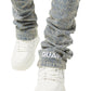 A person wears GUAPI Vintage Blue Distressed Cross Denim with rhinestone details, a "GUAPI" patch on one cuff, and white sneakers.