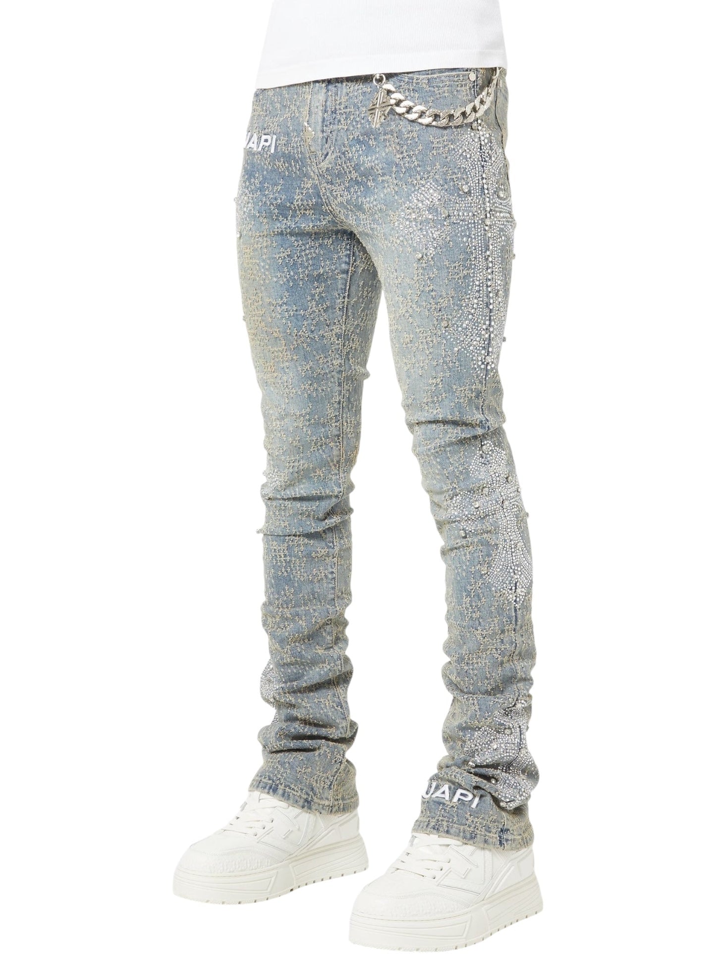 Person wearing GUAPI Guapi Vintage Blue Distressed Cross Denim jeans with chain detail, white sneakers, and a white top, shown from the waist down.