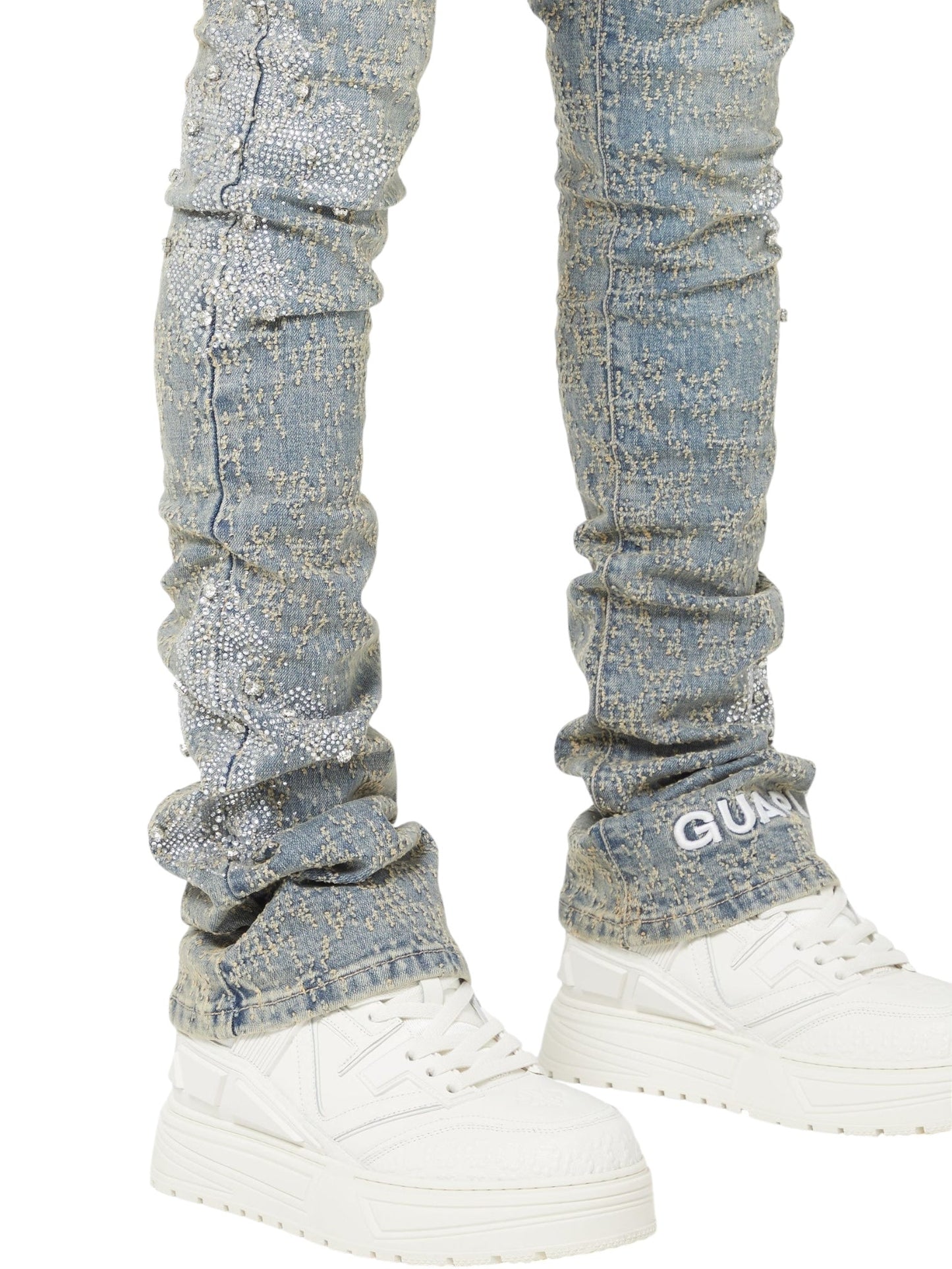 Wearing GUAPI Vintage Blue Distressed Cross Denim jeans with a textured skinny fit and white sneakers. Only the legs and feet are visible.
