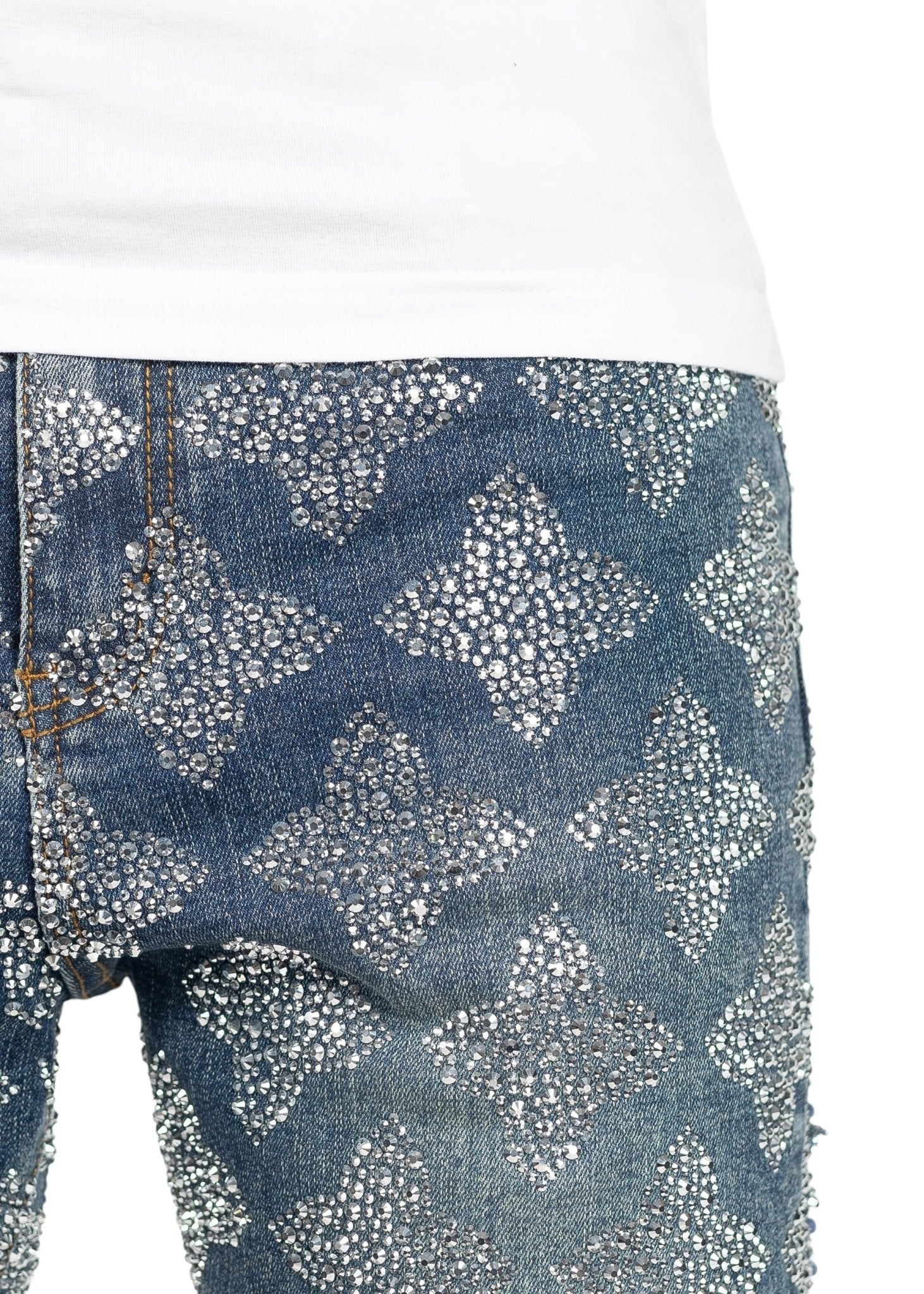 A close-up of GUAPI's Guapi Vintage Blue Embellished Denim jeans paired with a white shirt, featuring a slim-fit silhouette and a dazzling crystal-studded lattice pattern that forms sparkling diamond shapes.