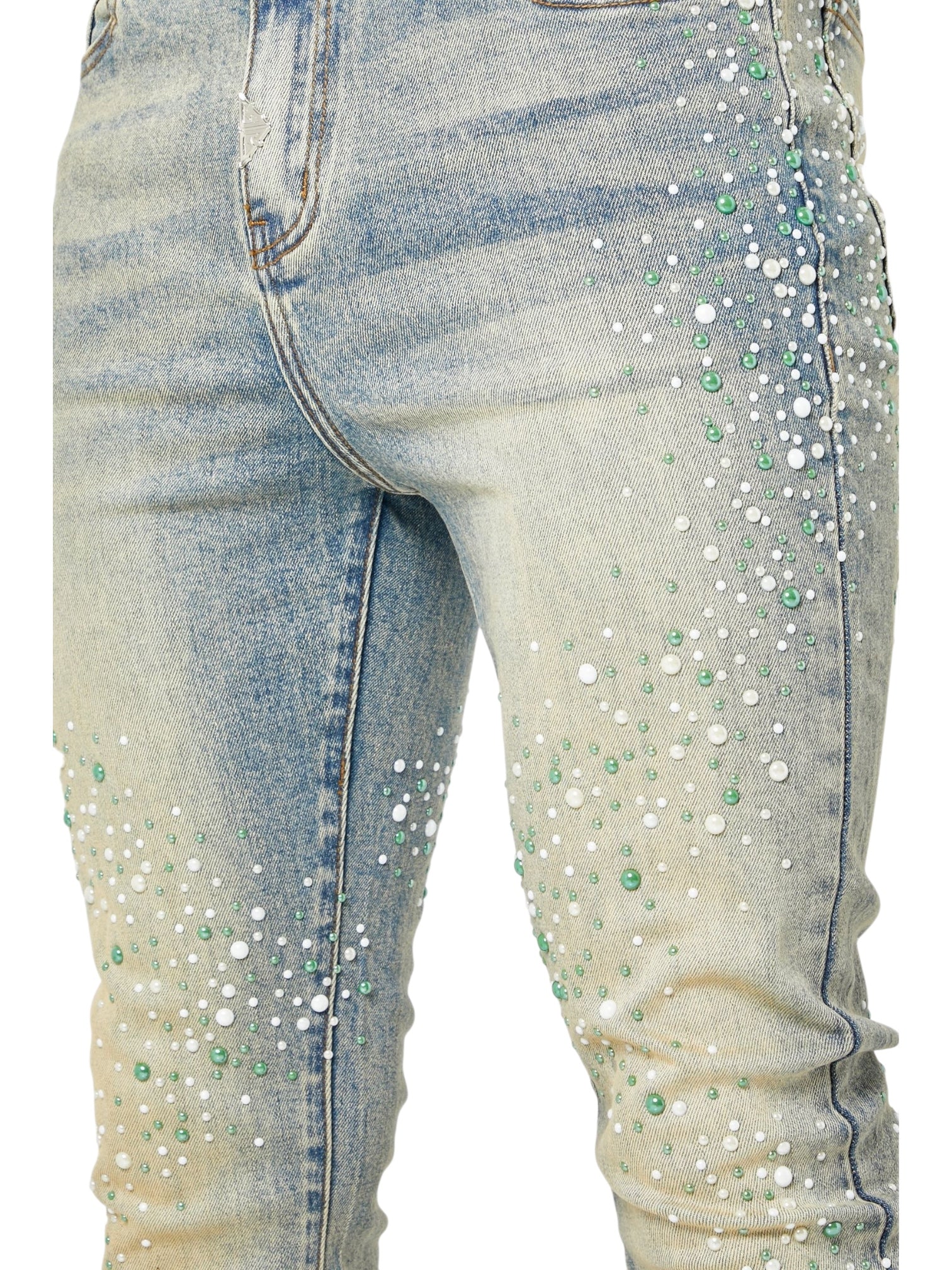 Close-up of GUAPI's Guapi Vintage Olive Pearls Denim skinny stacked jeans, detailed with scattered white and green bead embellishments on the front thigh and knee areas.