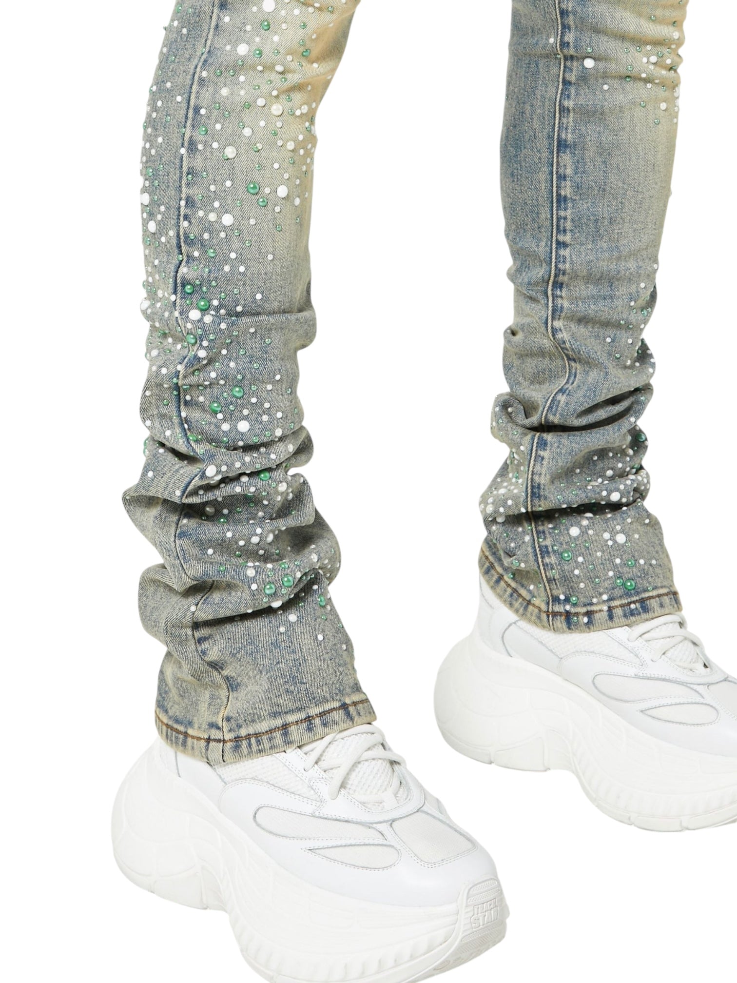 Person wearing GUAPI Vintage Olive Pearls Denim, featuring green, white, and pearl rhinestones, paired with white chunky sneakers—shown from the waist down.