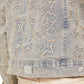 A close-up of the Guapi Vintage Stars Denim Jacket by GUAPI showcases its star embroidery design and metal tag, stylishly paired with light-colored pants.