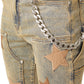 The Guapi Vintage Stars Denim V2 by GUAPI features brown patches and a silver chain on the hip. Designed for a slim fit with a stacked hem, these stylish jeans bring both chic comfort and elegance to any outfit.