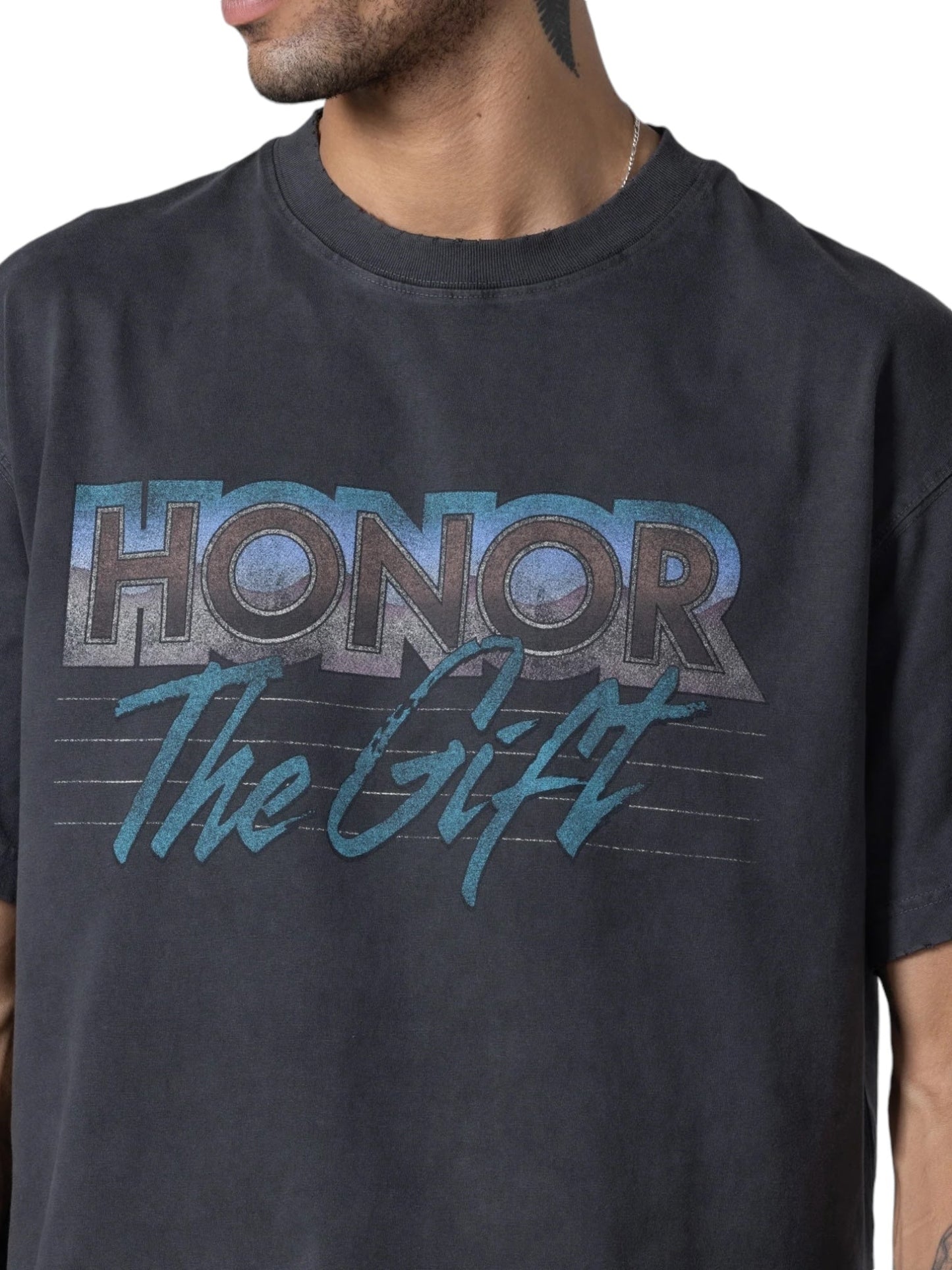 A man wears a black Honor The Gift After Hours T-shirt featuring "HONOR THE GIFT" in bold cursive, creating a vintage style.