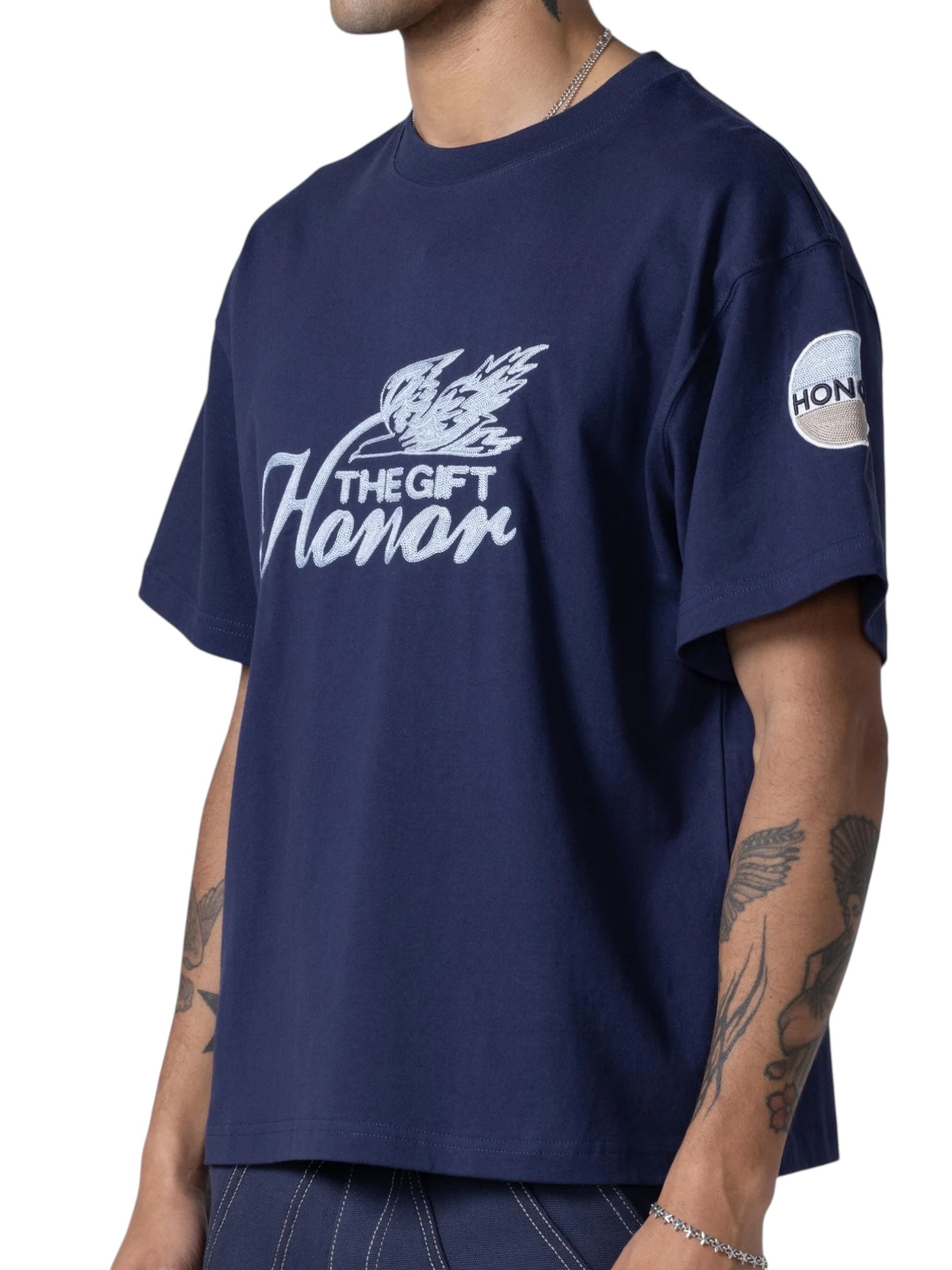A person wearing the HONOR THE GIFT Auto Club Box Tee Navy, a Standard Fit 100% Cotton t-shirt with "THE GIFT Honar" and bird graphic on the front, plus a round "HONAR" patch on the sleeve.