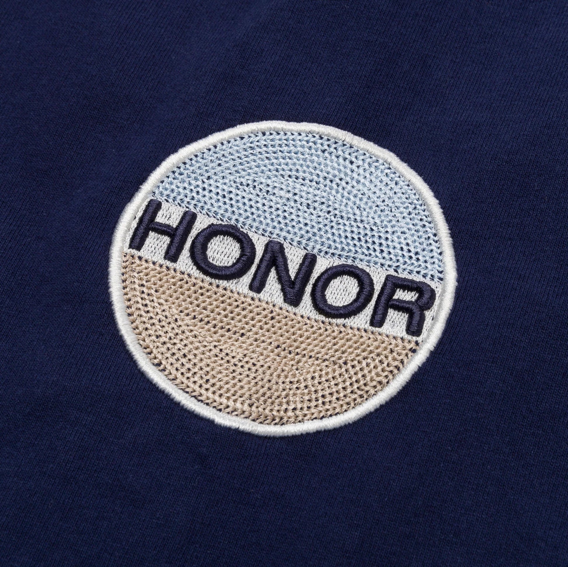 The "Honor The Gift Auto Club Box Tee Navy" by HONOR THE GIFT features a circular chain-stitched embroidered patch with "HONOR" on navy fabric, accented by light blue and beige segments.
