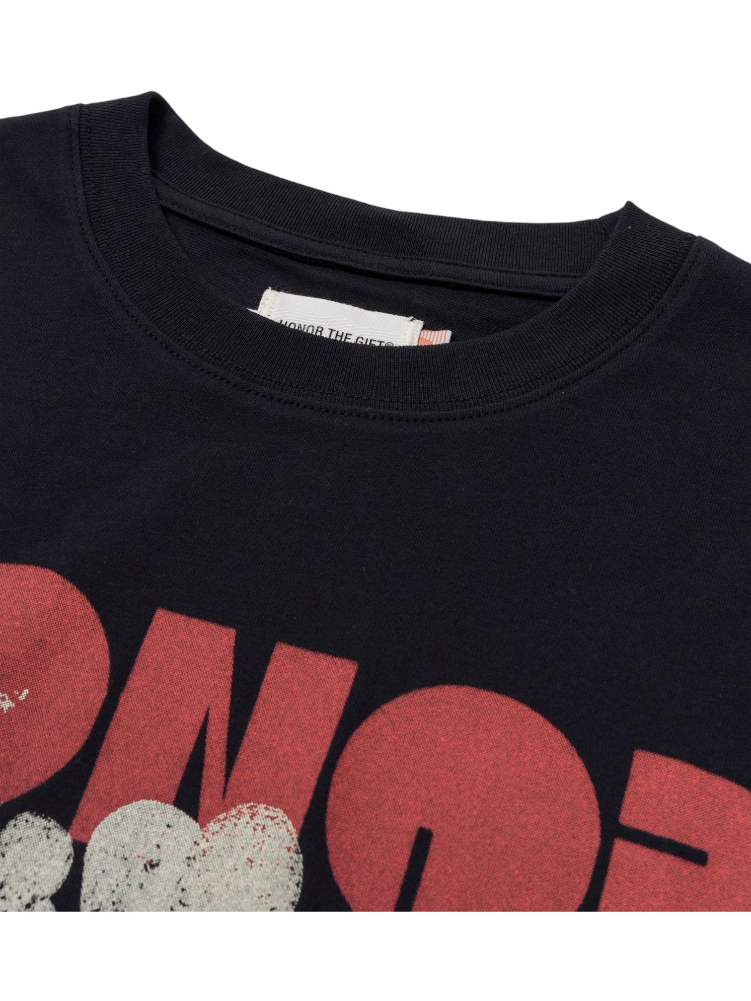 Close-up of the HONOR THE GIFT Block Party T-shirt in black, made from 100% cotton, with a sewn-in inner collar label and a bold red graphic partially visible.