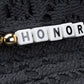White letter beads spelling "HONOR" and a gold bead are set on black fabric—perfect accents for the HONOR THE GIFT Friendship Crochet Bucket Hat Black by HONOR THE GIFT.