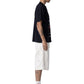 A man stands in profile wearing a black T-shirt, HONOR THE GIFT Gears Carpenter Short Cream with a 13" inseam and 100% cotton, paired with white socks and black high-top sneakers against a plain background.
