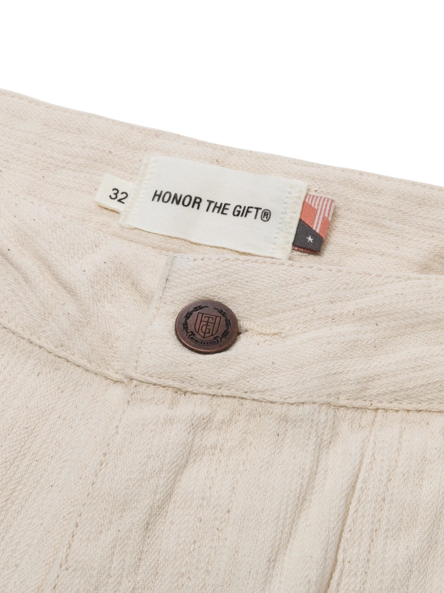 Close-up of Honor The Gift Gears Carpenter Short Cream by HONOR THE GIFT, featuring a beige twill waistband, brown button, "HONOR THE GIFT®" label with size 32 tag, 13" inseam, small flag detail, and crafted from 100% cotton.