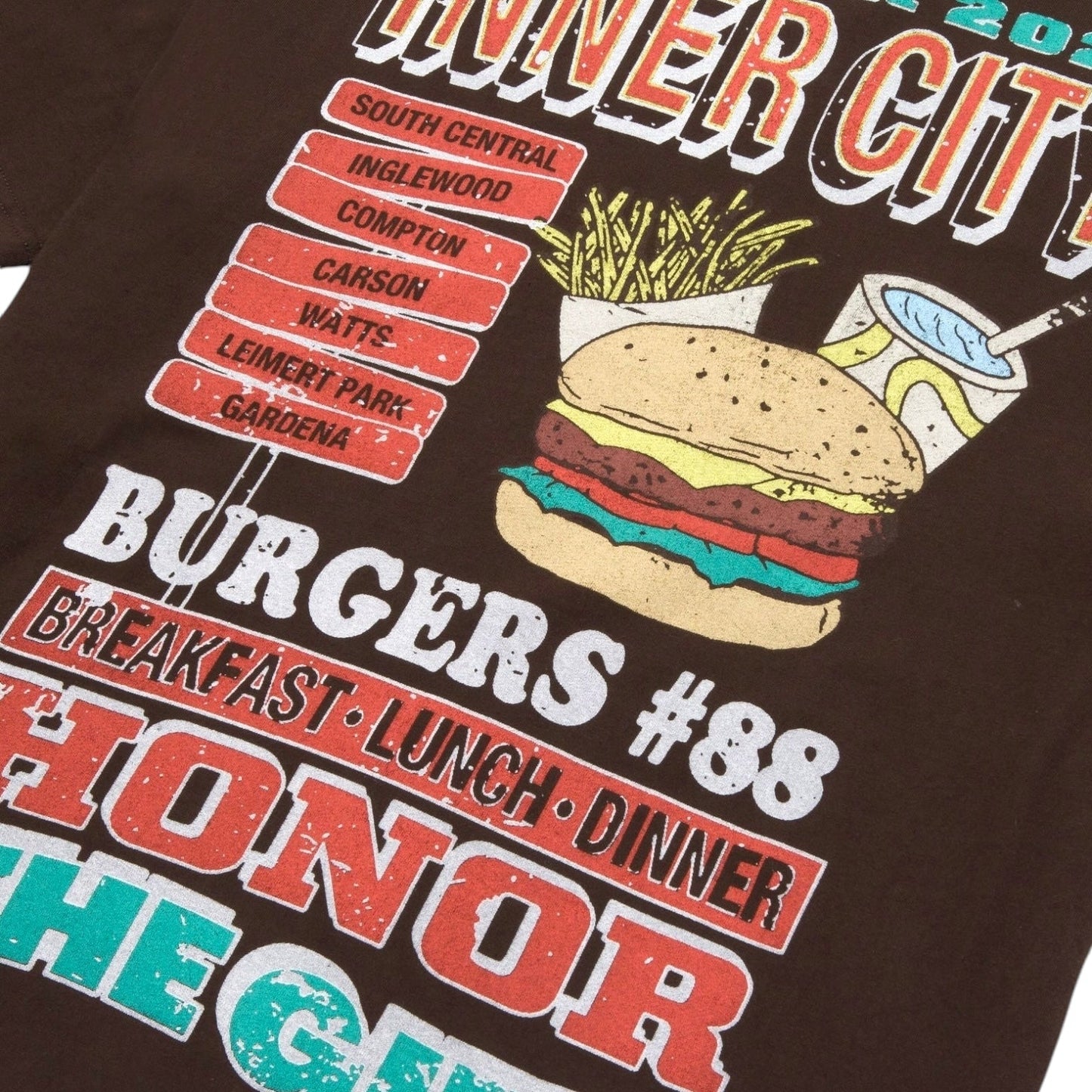 Made from 100% cotton, the Honor The Gift HTG Burgers SS Tee in black features a garment-dyed finish with striking text and graphics showcasing a hamburger, fries, drink, and city names like Inglewood and Compton. It includes a vintage pocket design adorned with phrases such as "Honor the G" and "Burgers #88 Breakfast Lunch Dinner," proudly representing the HONOR THE GIFT brand.