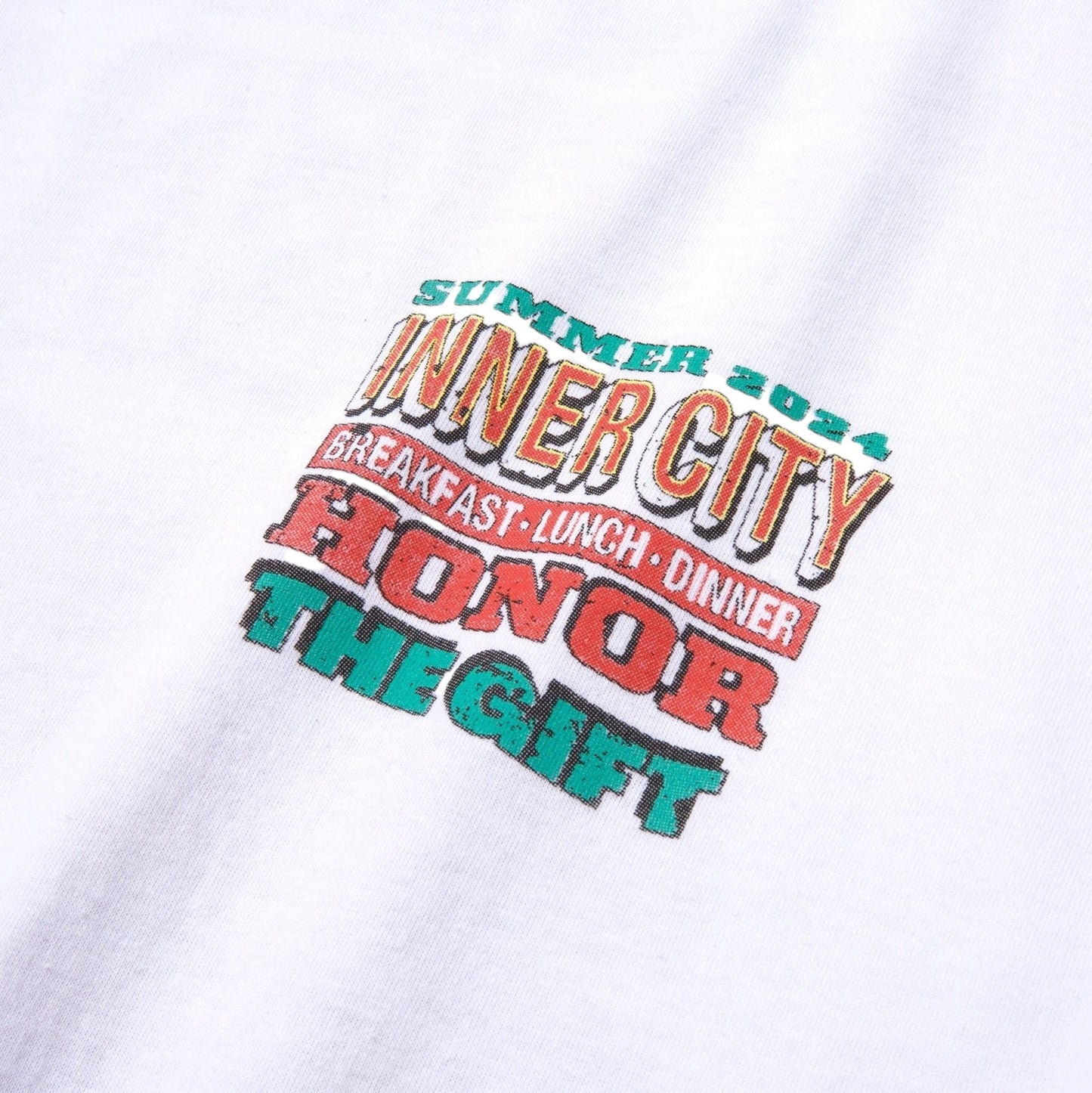 The Honor The Gift Htg Burgers Ss Tee White, by HONOR THE GIFT, is crafted from 100% cotton and showcases a vibrant text design: "Summer 2024, Inner City, Breakfast Lunch Dinner, Honor The Gift." This garment-dyed tee offers a soft feel and timeless appeal.