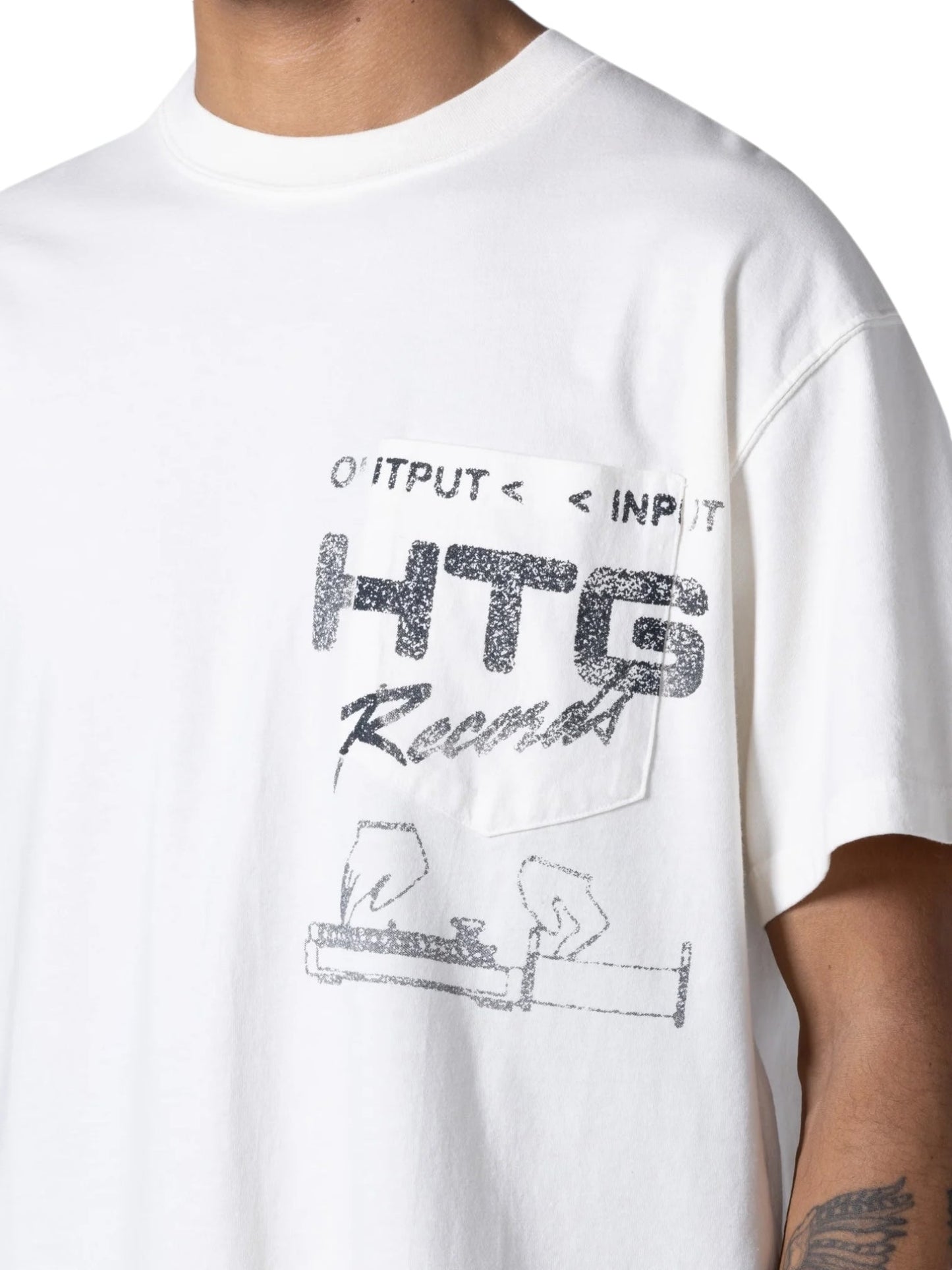 A person wearing the HONOR THE GIFT HTG RECORDS TEE WHITE, crafted from 100% cotton, showcasing "OUTPUT < INPUT HTG Record" along with an illustration of a turntable. The T-shirt has a vintage wash and features distressed custom artwork, offering a unique, retro vibe.