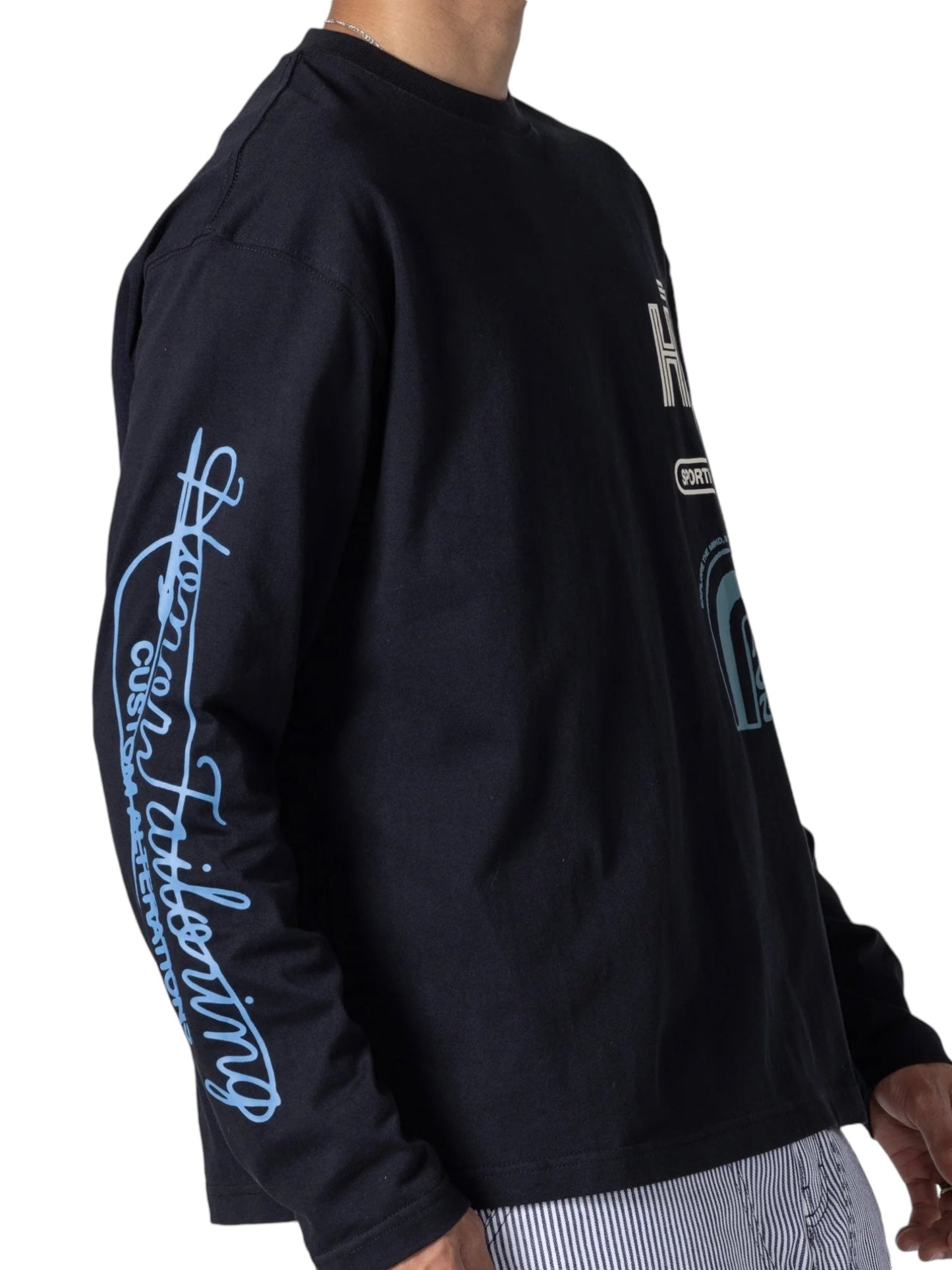 Wearing the Honor The Gift Mall LS T-shirt Black, crafted from 100% cotton and featuring light blue graphic designs with mall logos on the sleeve, a person embodies style and comfort through this HONOR THE GIFT fashion-forward heavyweight jersey.