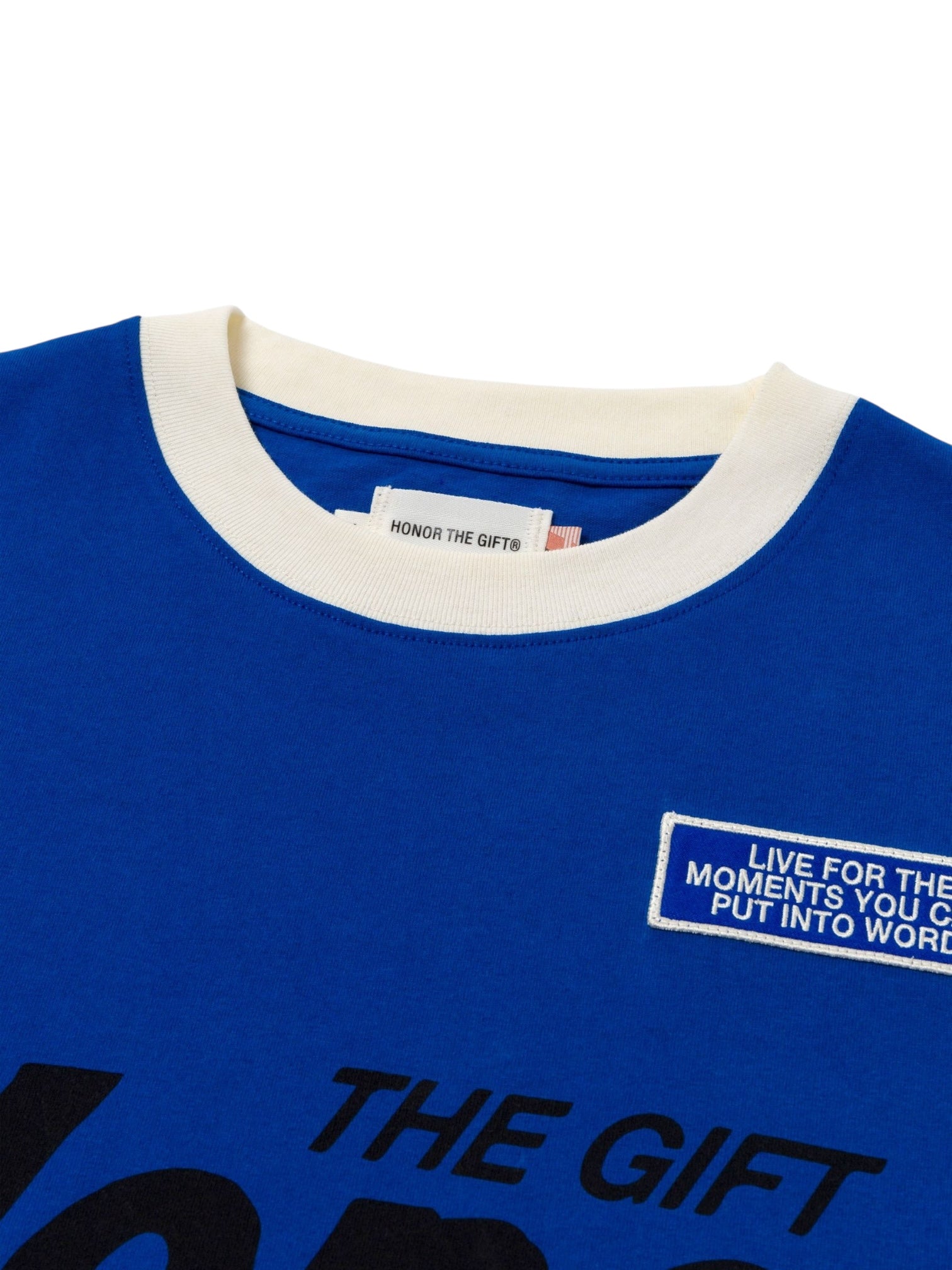 Close-up of the HONOR THE GIFT Multi Box Tee in blue, featuring a white collar, brand label, and a patch reading "LIVE FOR THE MOMENTS YOU CAN PUT INTO WORDS.