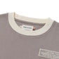 Close-up of the HONOR THE GIFT Multi Box Tee Stone, a gray heavyweight cotton t-shirt with a white collar, visible tags, and a patch reading "LIVE FOR THE MOMENTS YOU CAN’T PUT INTO WORDS." Blue text adds a touch of style to this durable piece.