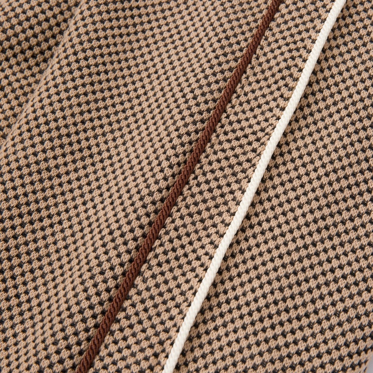 The detailed flat embroidery is showcased on the Honor The Gift Novelty Knit Track Jacket Brown by HONOR THE GIFT, with a close-up of its brown and beige houndstooth patterned fabric that highlights a prominent seam and white trim.