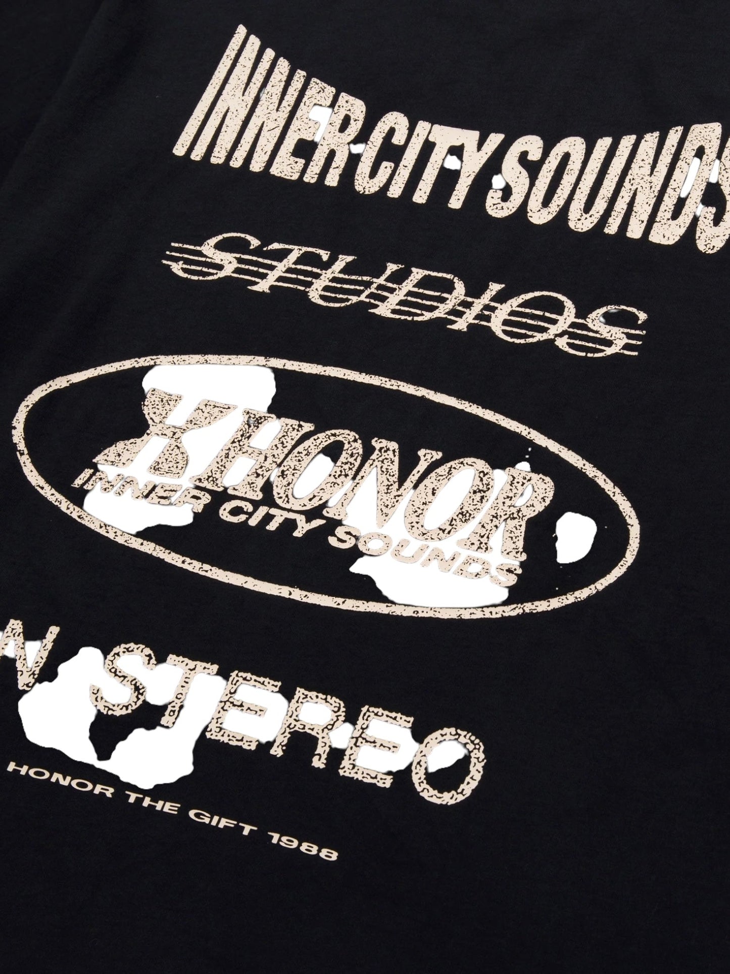 The HONOR THE GIFT STUDIO TEE BLACK by HONOR THE GIFT features black fabric with white, distressed text including phrases such as “INNER-CITY SOUNDS STUDIOS,” “HONOR,” and “IN STEREO.” The artwork appears worn and faded in some areas, crafted on soft, heavyweight cotton jersey for a custom studio print look.