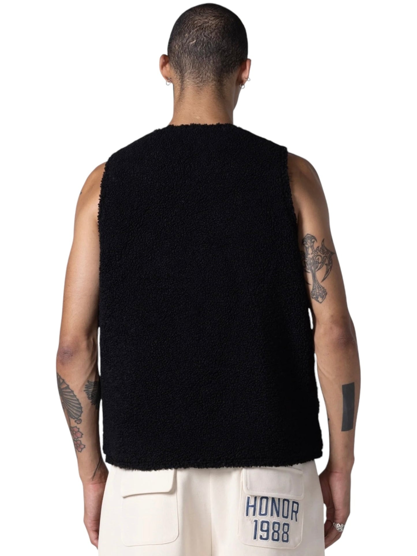 A person with short hair and tattoos on both arms is wearing a HONOR THE GIFT TEDDY NOTES VEST BLACK and white pants with "HONOR 1988" written on the right pocket, facing away from the camera.