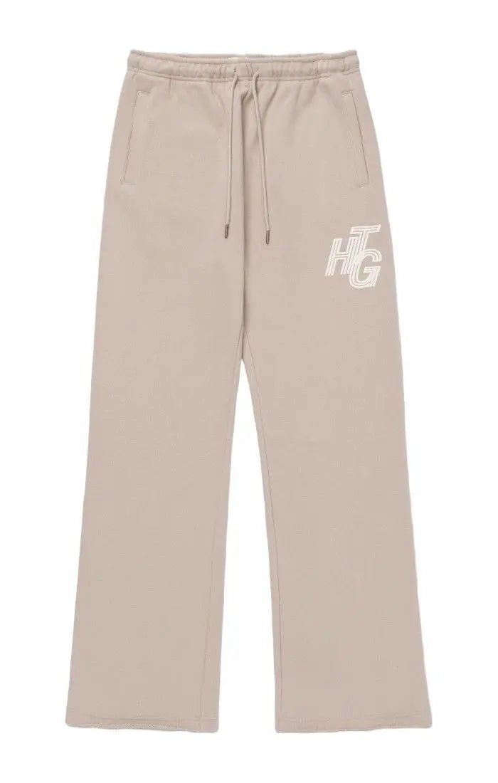 The Honor The Gift Terry HTG Sweatpant Stone by HONOR THE GIFT is made from 100% cotton in beige, featuring a drawstring waist, two front pockets, and the "HTG" initials on the left thigh.