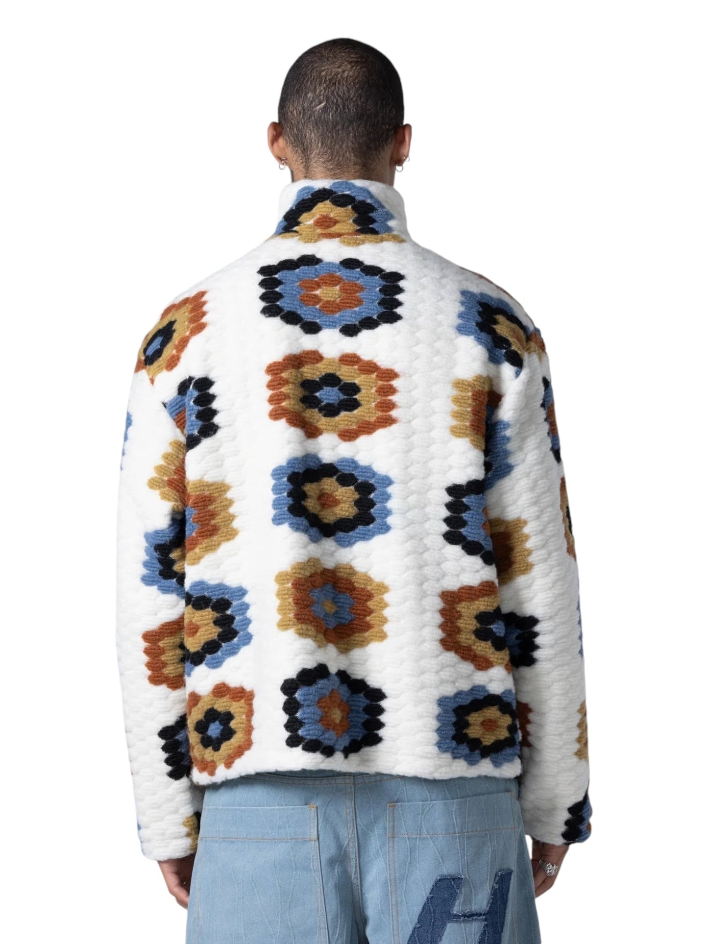 A person is standing with their back to the camera, wearing the HONOR THE GIFT TEXTURED FULL ZIP Cream jacket from HONOR THE GIFT, which features a festival-inspired design with a colorful, symmetrical geometric pattern and light blue pants. The jacket includes a full zip closure for added convenience.