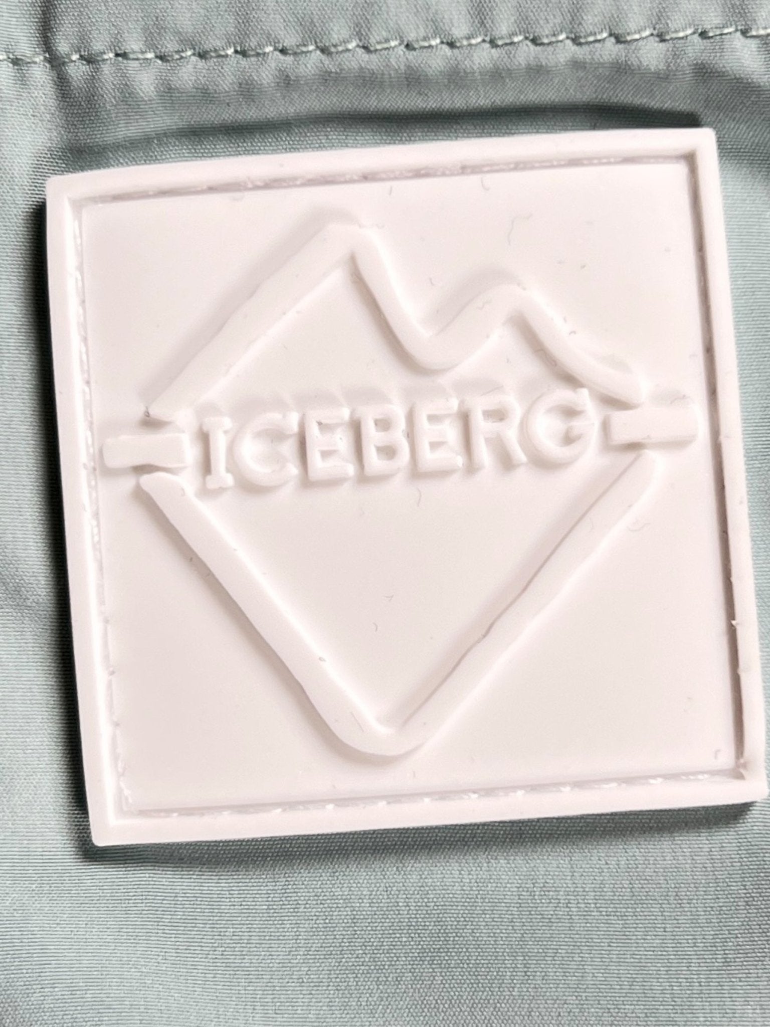 A white rubber "ICEBERG" patch with an abstract iceberg design is sewn onto the light mint 100% polyester fabric of the Iceberg ICE25MBM01 Medium Boardshort, echoing classic brand swim trunk details.