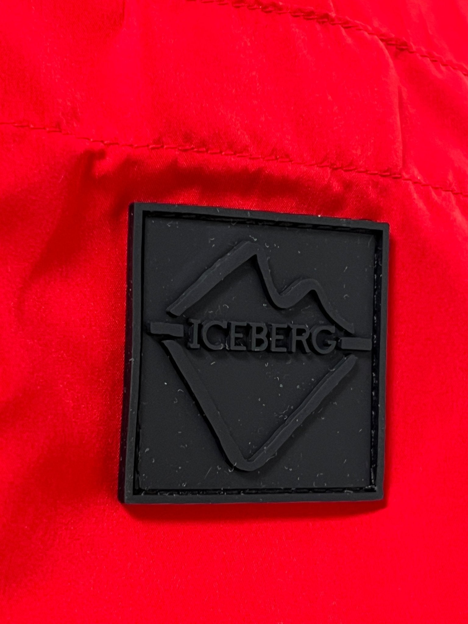A black rectangular patch with "ICEBERG" and a mountain outline is sewn onto the bright red ICEBERG ICE25MBM01 Medium Boardshort, made from 100% polyester.
