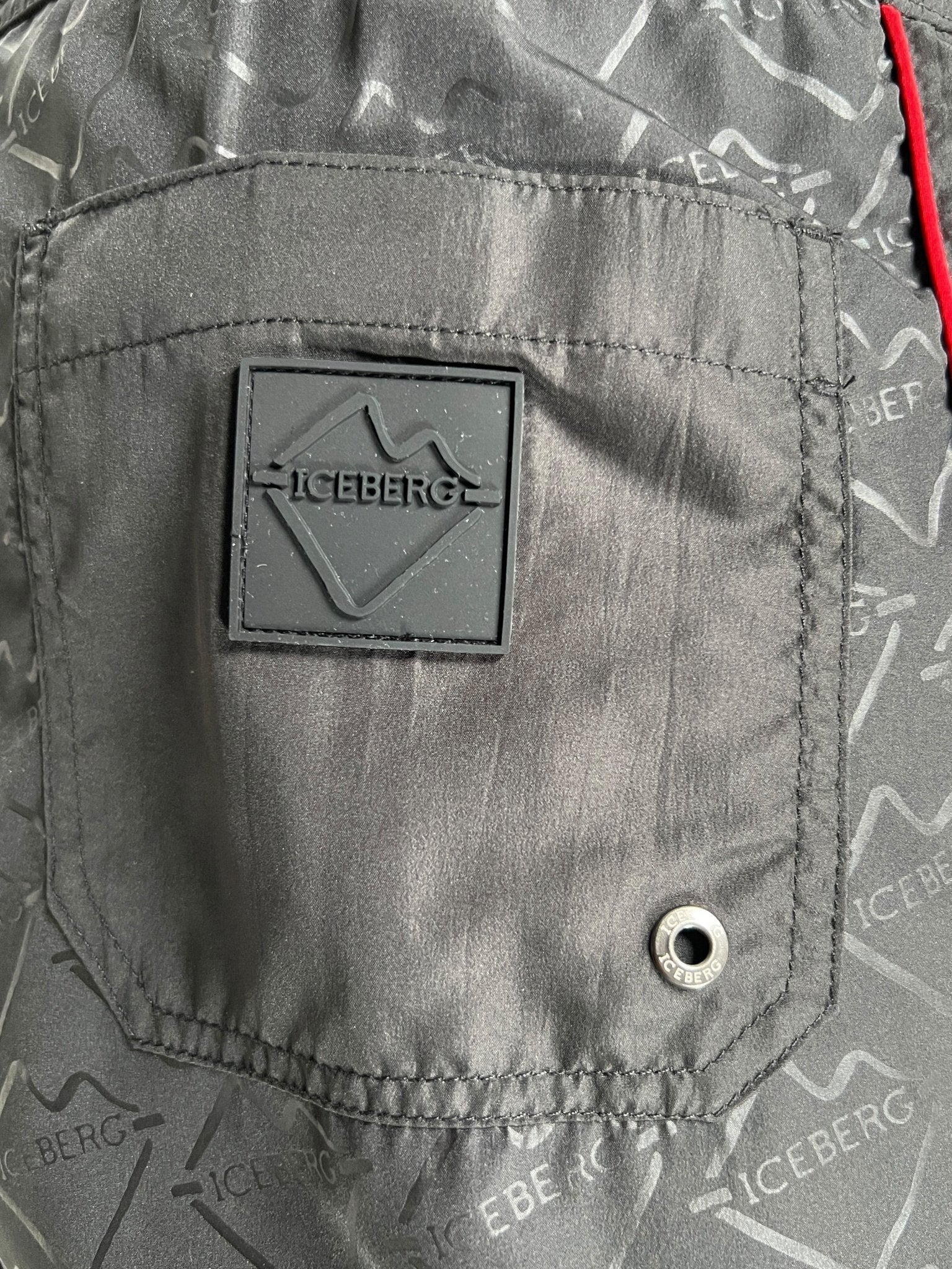 Close-up of the black polyester pocket on ICEBERG's ICE25MBS05 Short Boardshort, featuring a rubber ICEBERG patch logo, metal grommet, and repeating brand pattern. Imported.