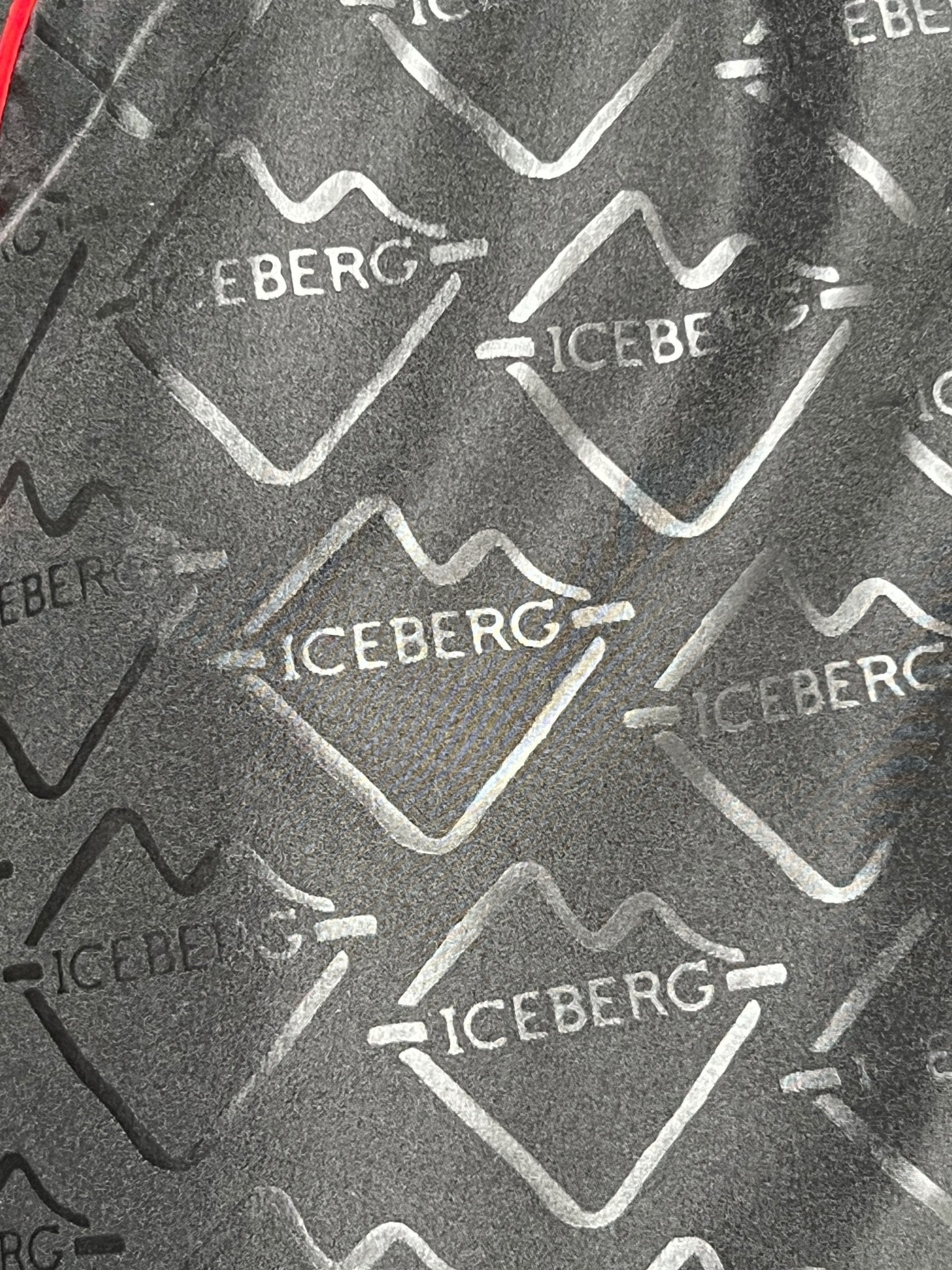 Close-up of the textured polyester fabric from the Iceberg ICE25MBS05 Short Boardshort Black, featuring a repeated "ICEBERG" logo and mountain outline in monochrome, by ICEBERG.