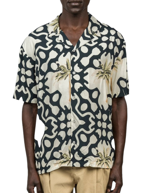 Someone dressed in the Inimigo ISH3525 Palm Shirt Black by INIMIGO, a short-sleeved button-up with abstract shapes and palm trees for a tropical vibe, paired with beige pants.