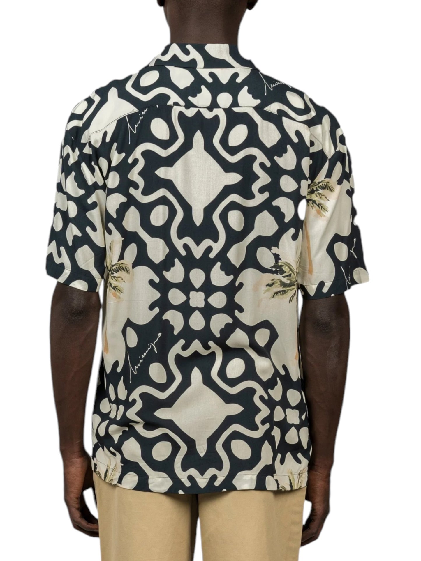 A person showcases a tropical vibe wearing the Inimigo ISH3525 Palm Shirt Black, featuring abstract black and white designs with subtle palm trees from the INIMIGO collection, paired with beige pants. The back view is shown.